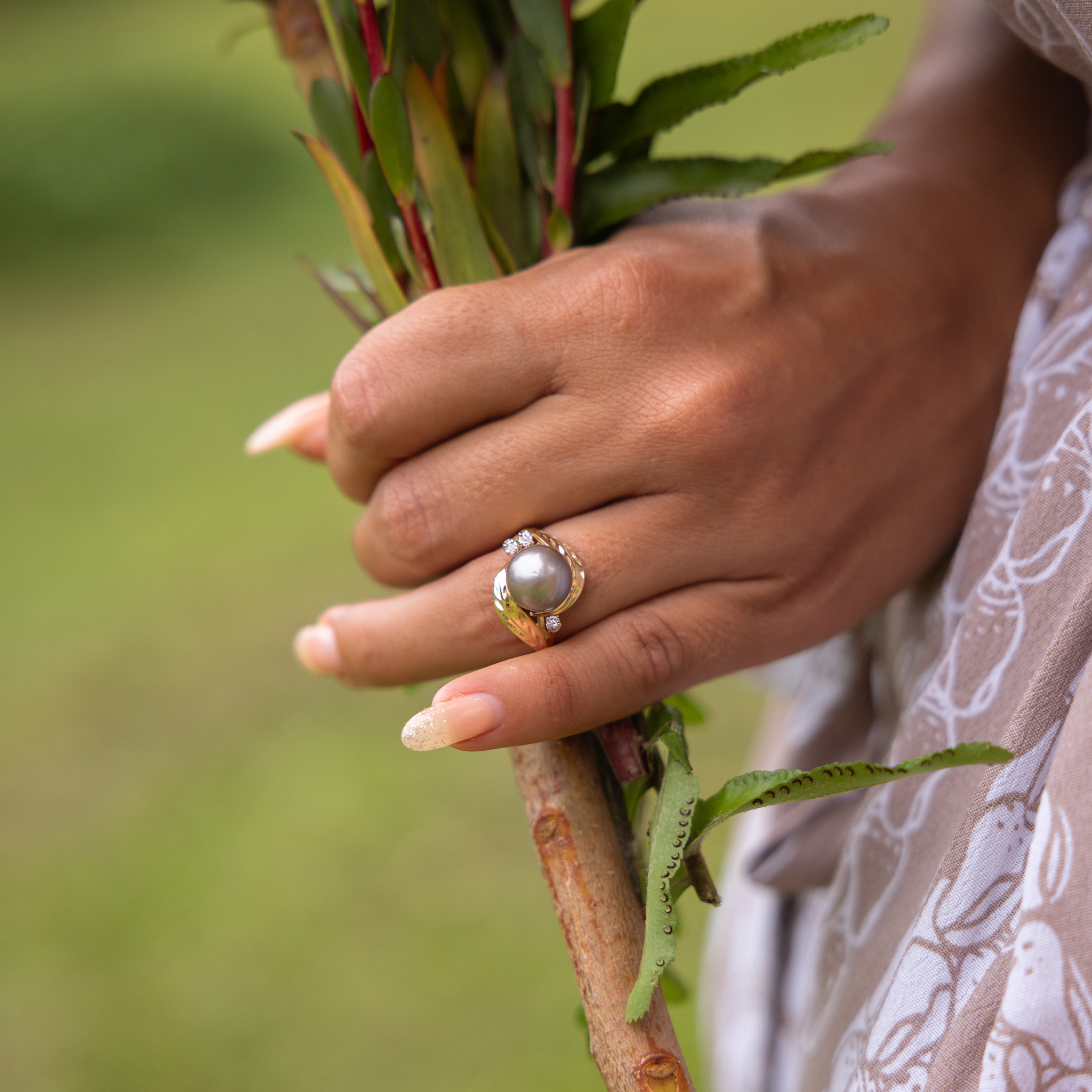 A hand with a maile leaf Tahitian black pearl ring holding the stems of a bouquet.