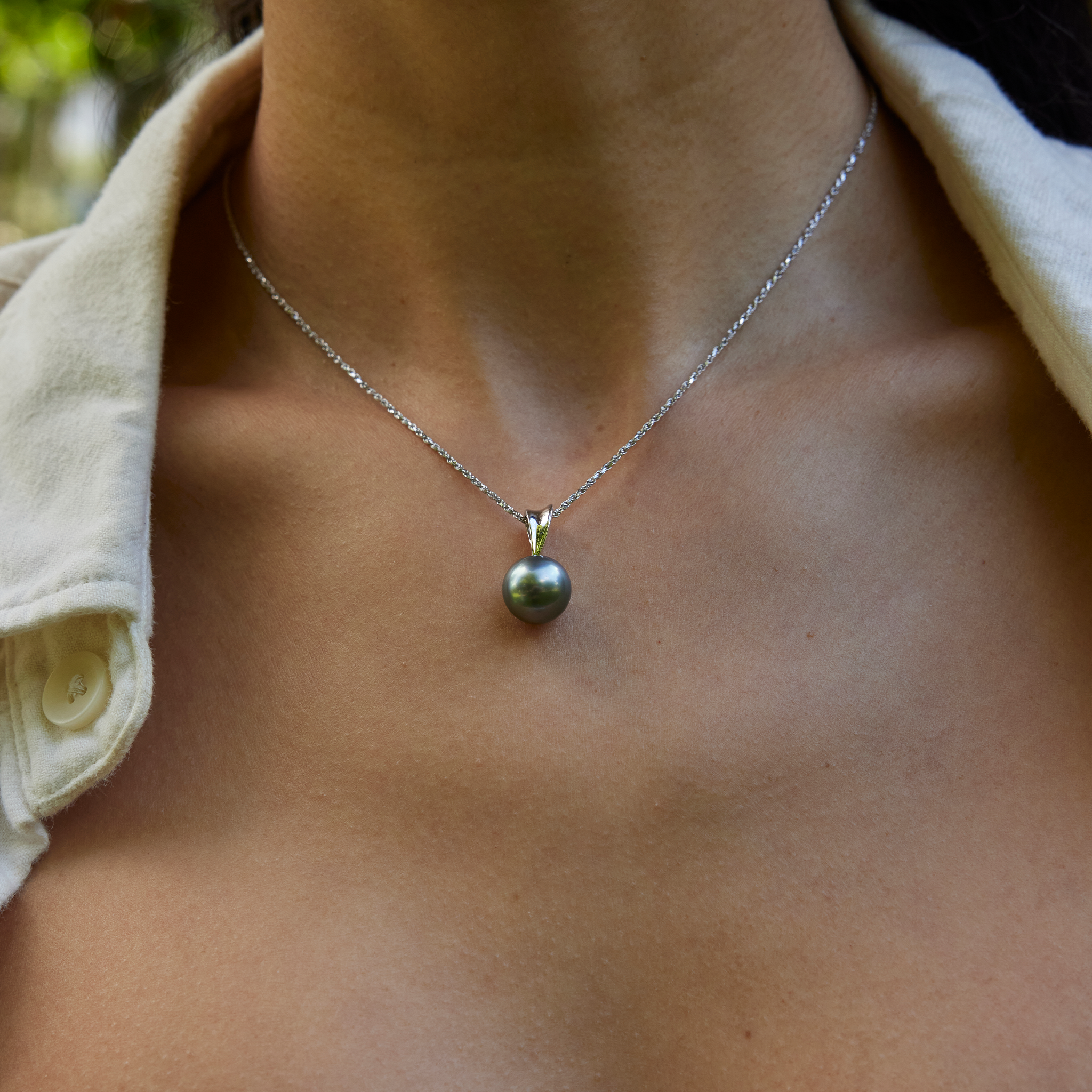 Tahitian black pearl pendant in 14k white gold, set on a raso chain, resting on a woman's neck.