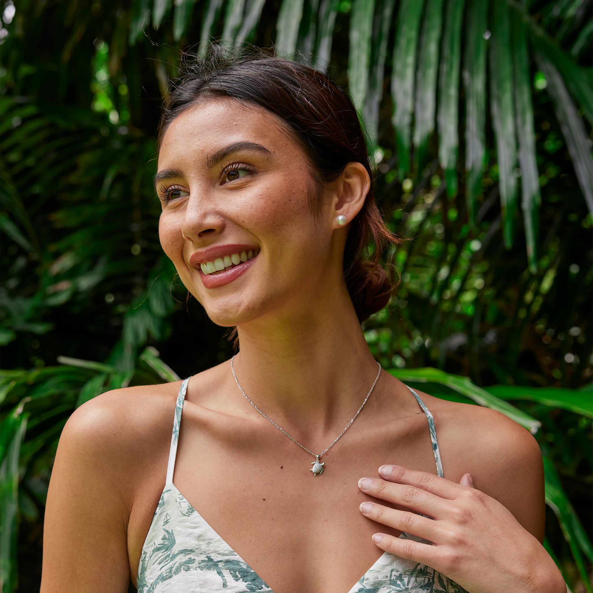 Smiling woman in a green patterned dress wearing an Akoya white pearl earring and diamond Honu pendant.