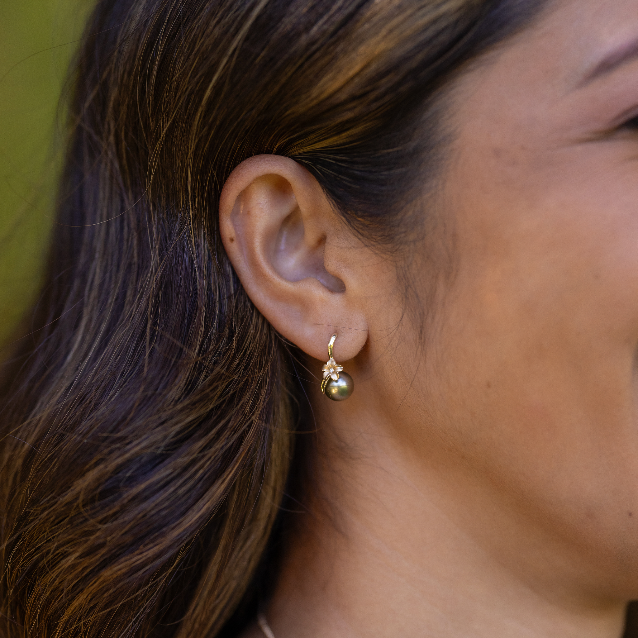 Close-up of a woman wearing a plumeria Tahitian black pearl earring.
