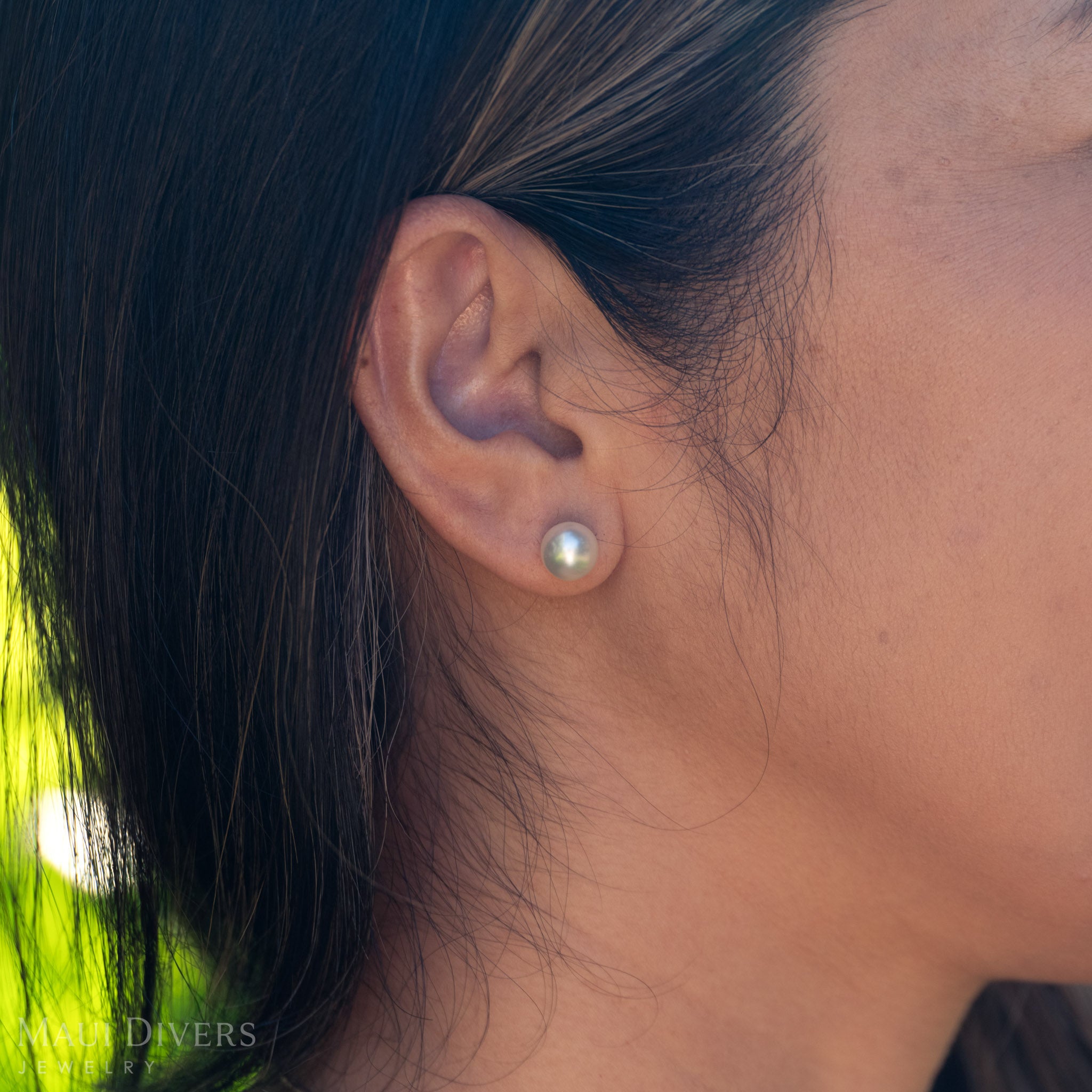Close-up of an ear with a South Sea white pearl earring, blurred green background