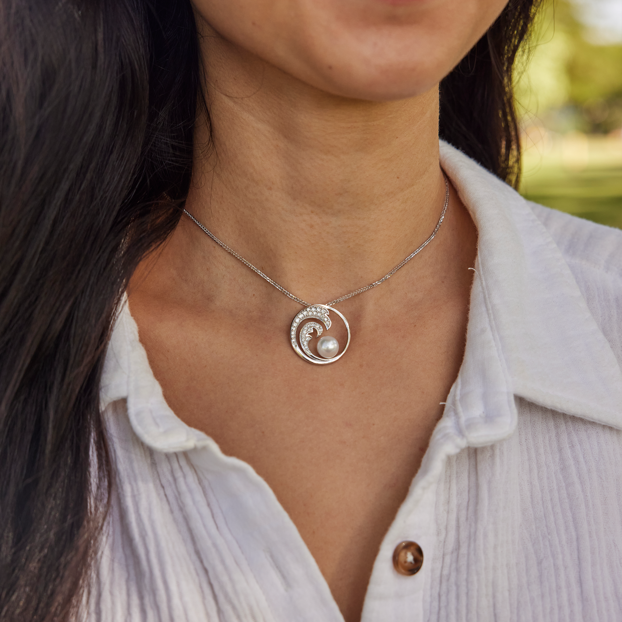 Close up of a woman in a white shirt wearing an white gold diamond wave pendant with an Akoya pearl