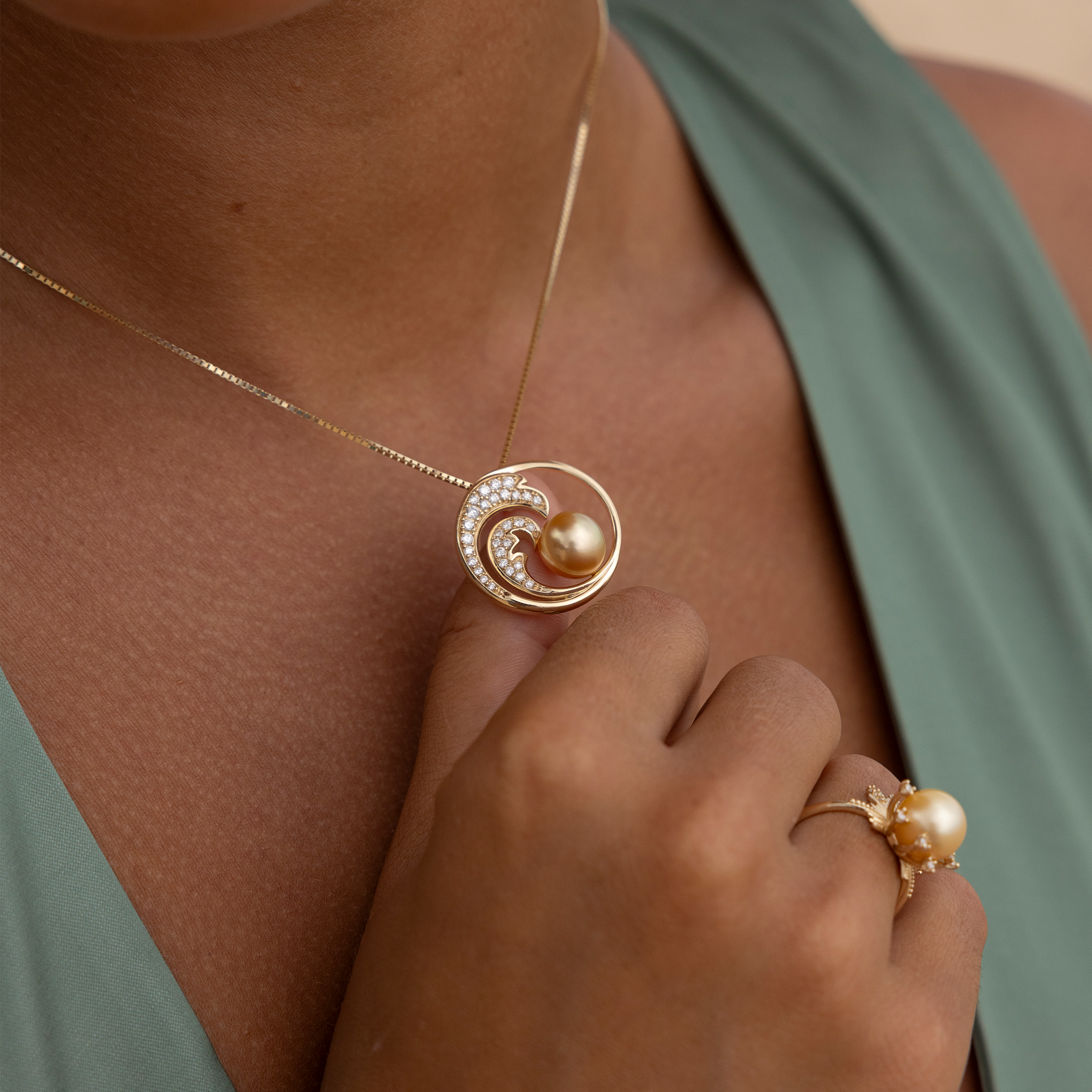Close up of a woman wearing a gold diamond wave South Sea gold pearl pendant on a box chain