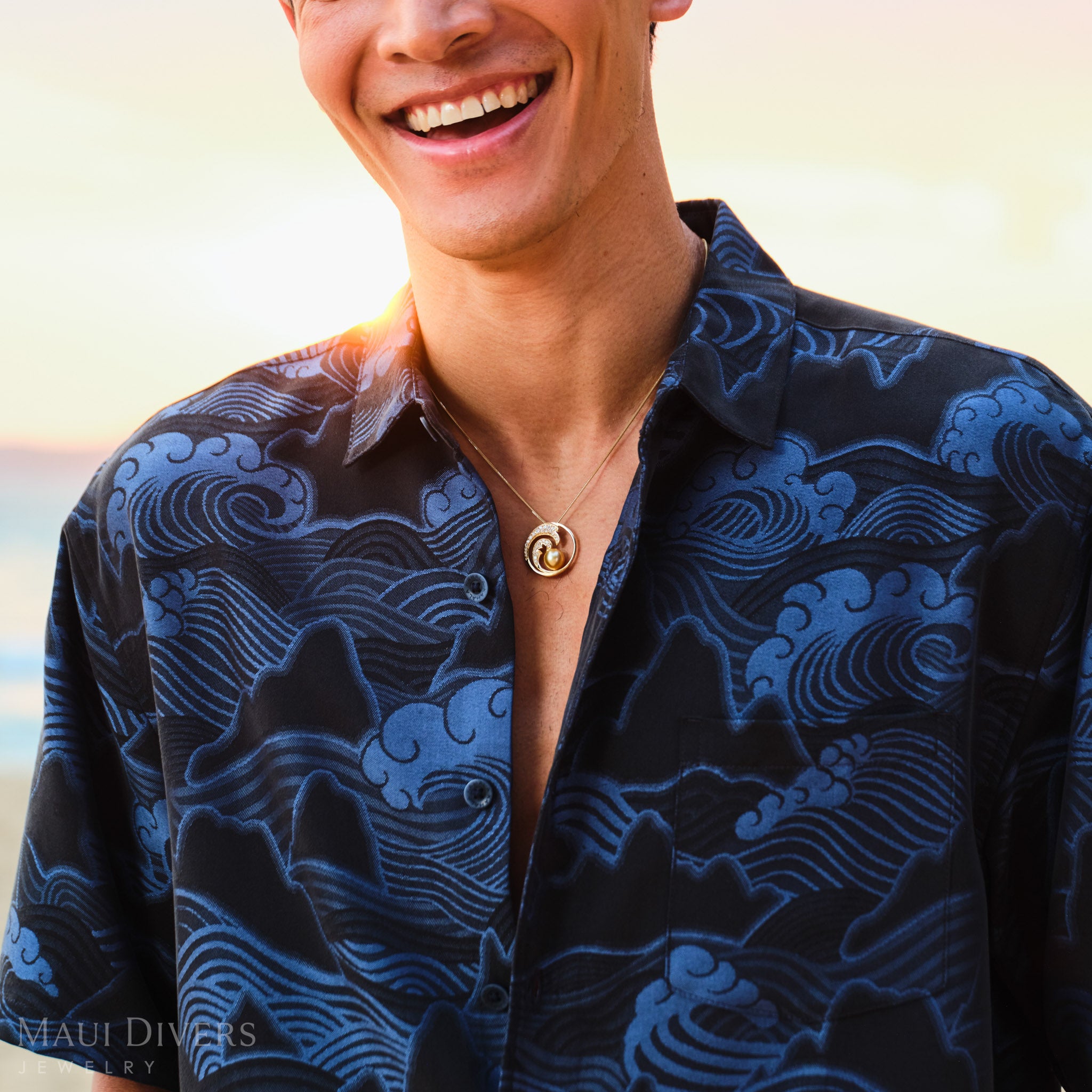 Man wearing a blue patterned shirt wearing a gold diamond wave South Sea gold pearl pendant with a blurred background