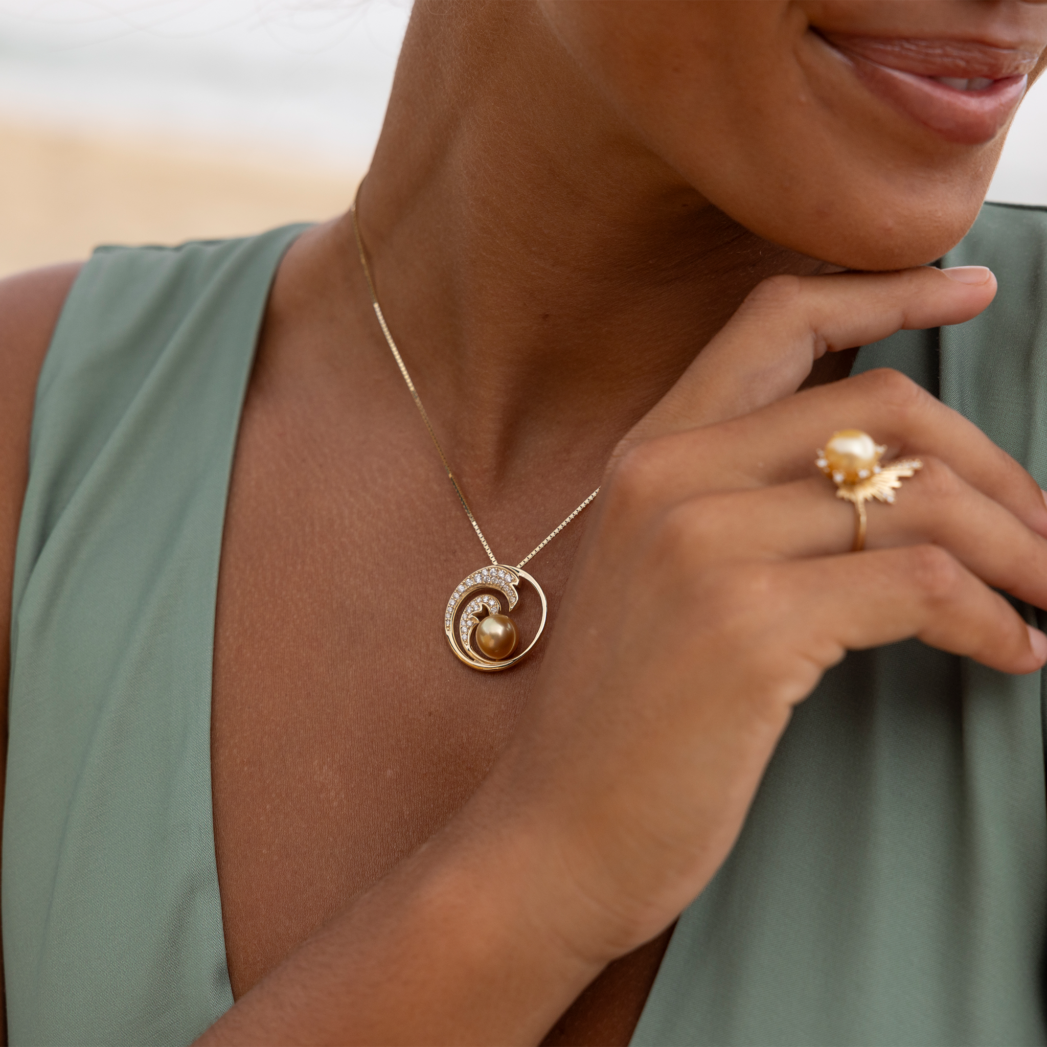Close up of a smiling woman wearing a gold diamond wave South Sea gold pearl pendant on a box chain