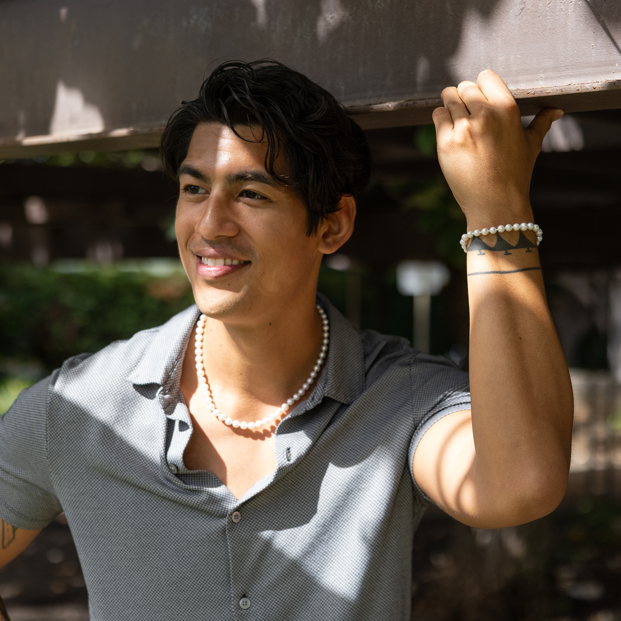 Smiling man wearing an Akoya white pearl strand necklace and bracelet against a blurred background