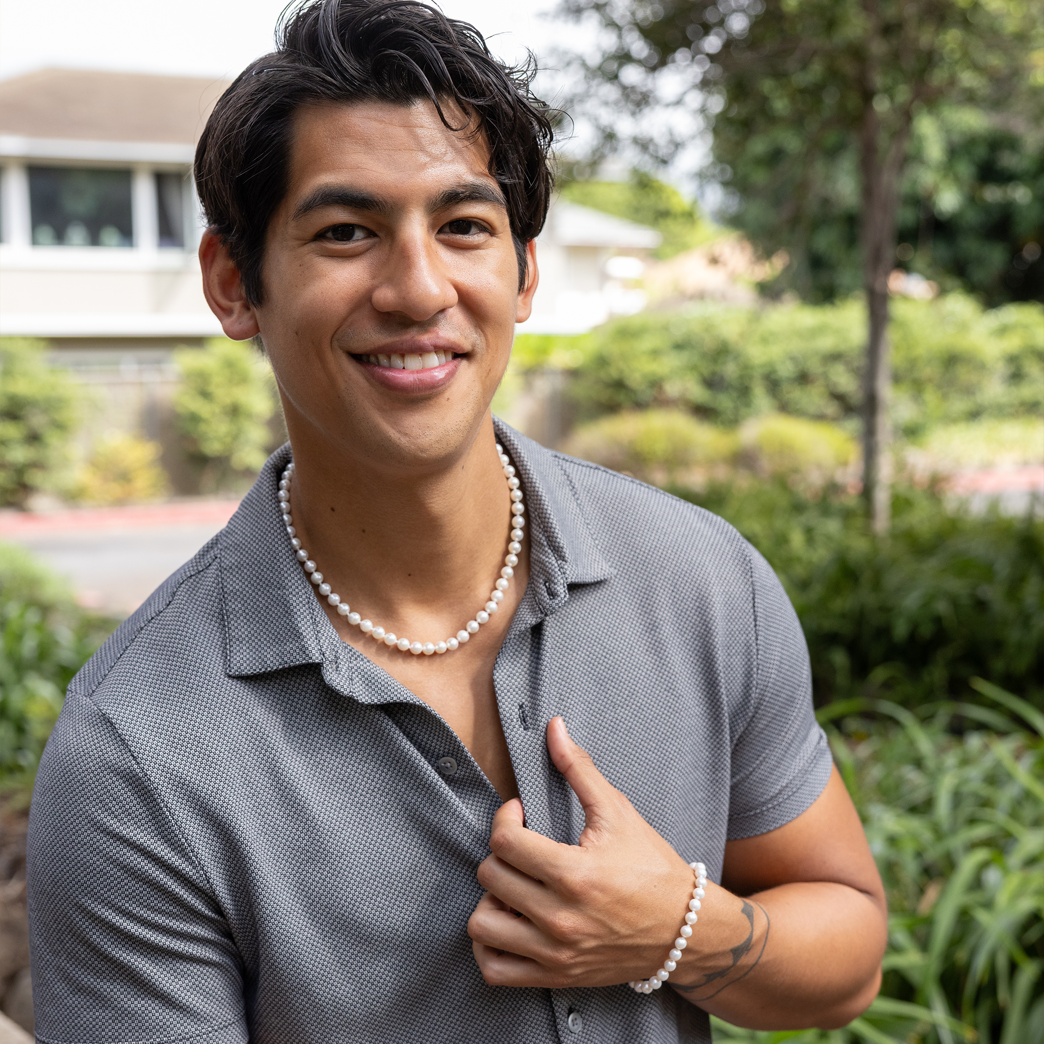 Smiling man wearing an Akoya white pearl strand necklace and bracelet in front of a blurred background