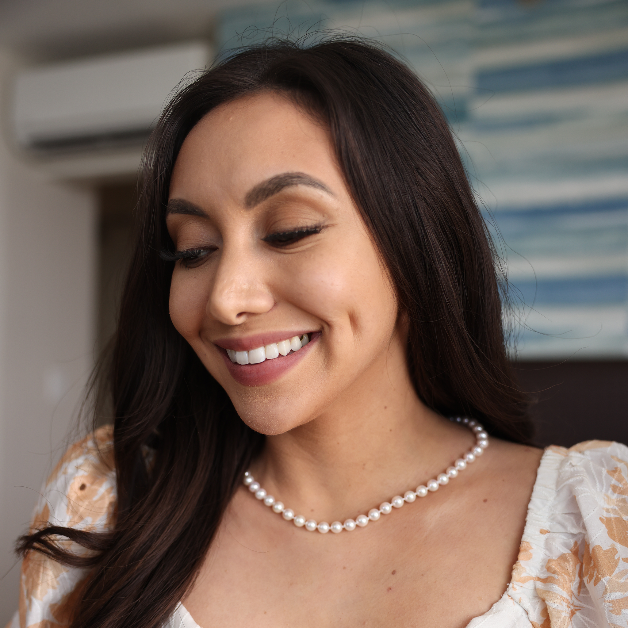 Close-up of a woman smiling wearing an Akoya white pearl strand necklace in front of a blurred background