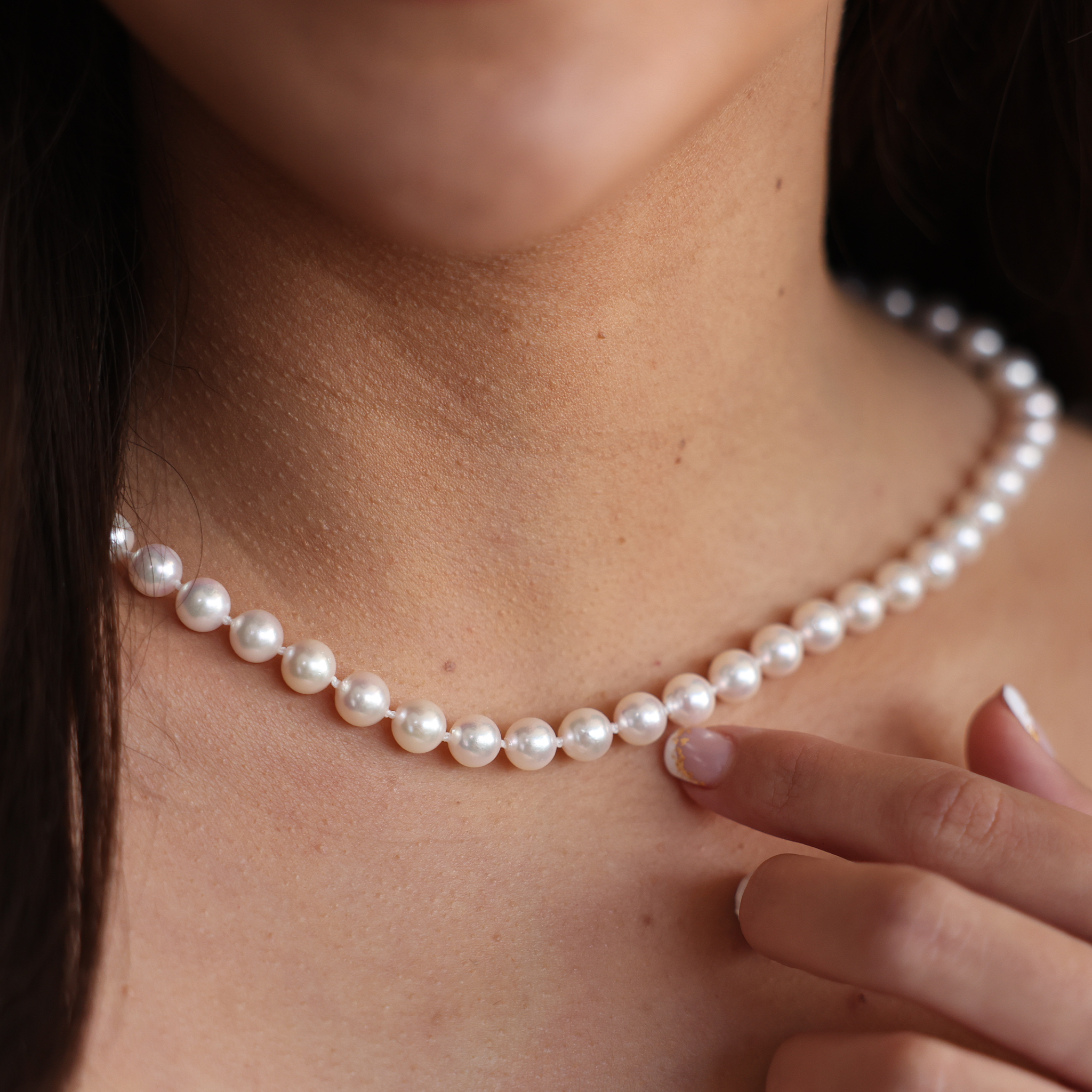 Close-up of a woman pointing to an Akoya white pearl strand necklace around her neck