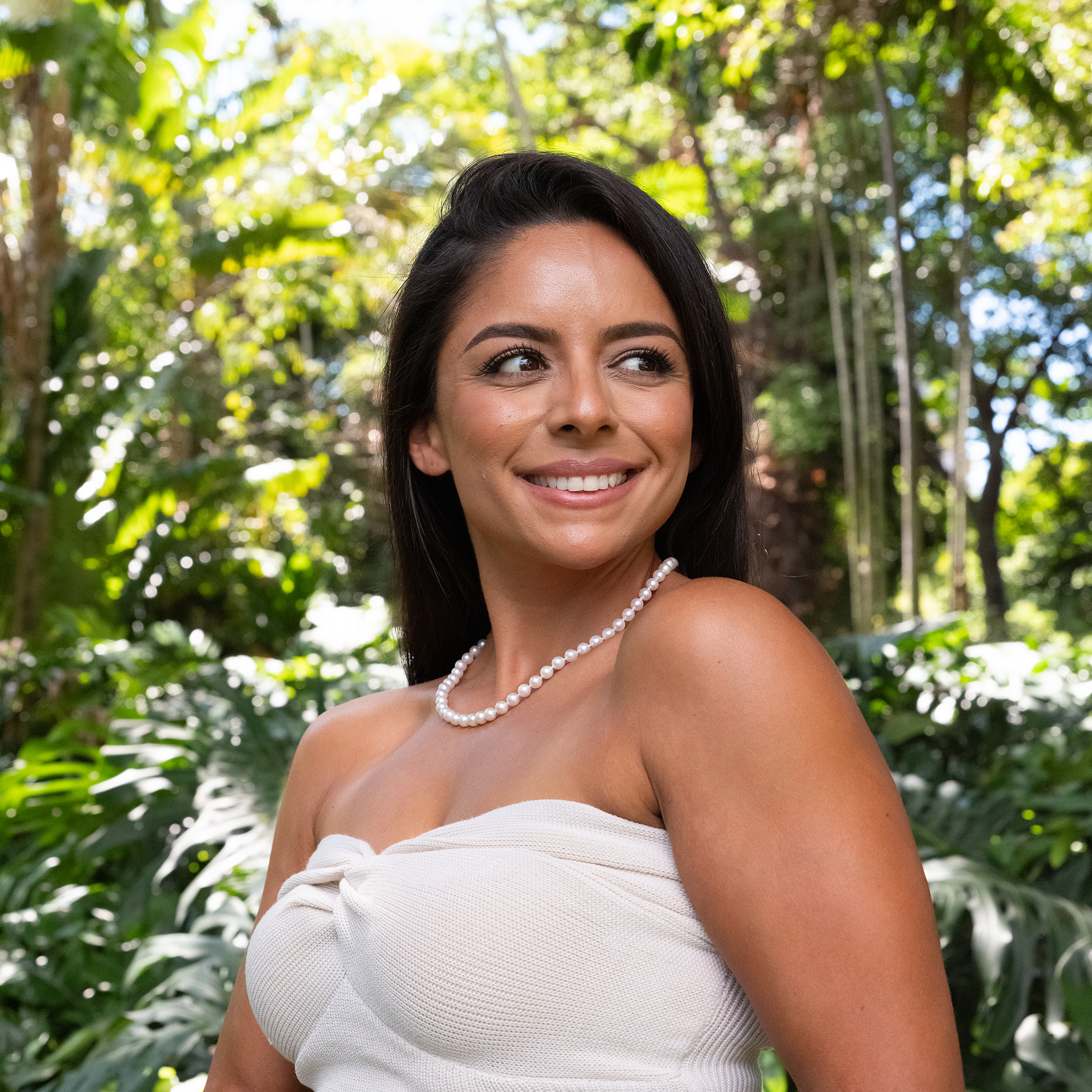 Woman smiling wearing an Akoya white pearl strand necklace in front of a blurred background
