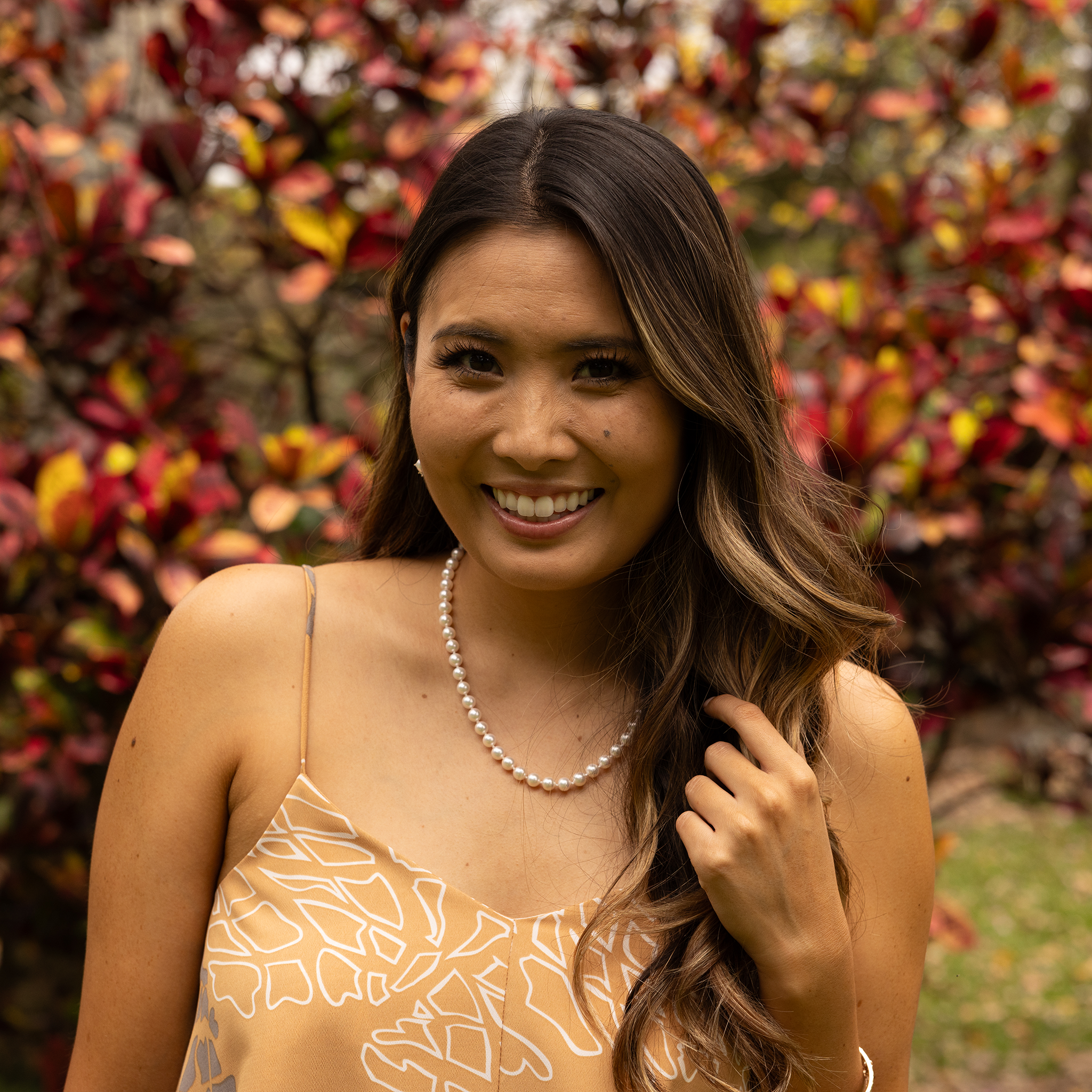 Smiling woman wearing an Akoya white pearl strand necklace in front of a blurred background