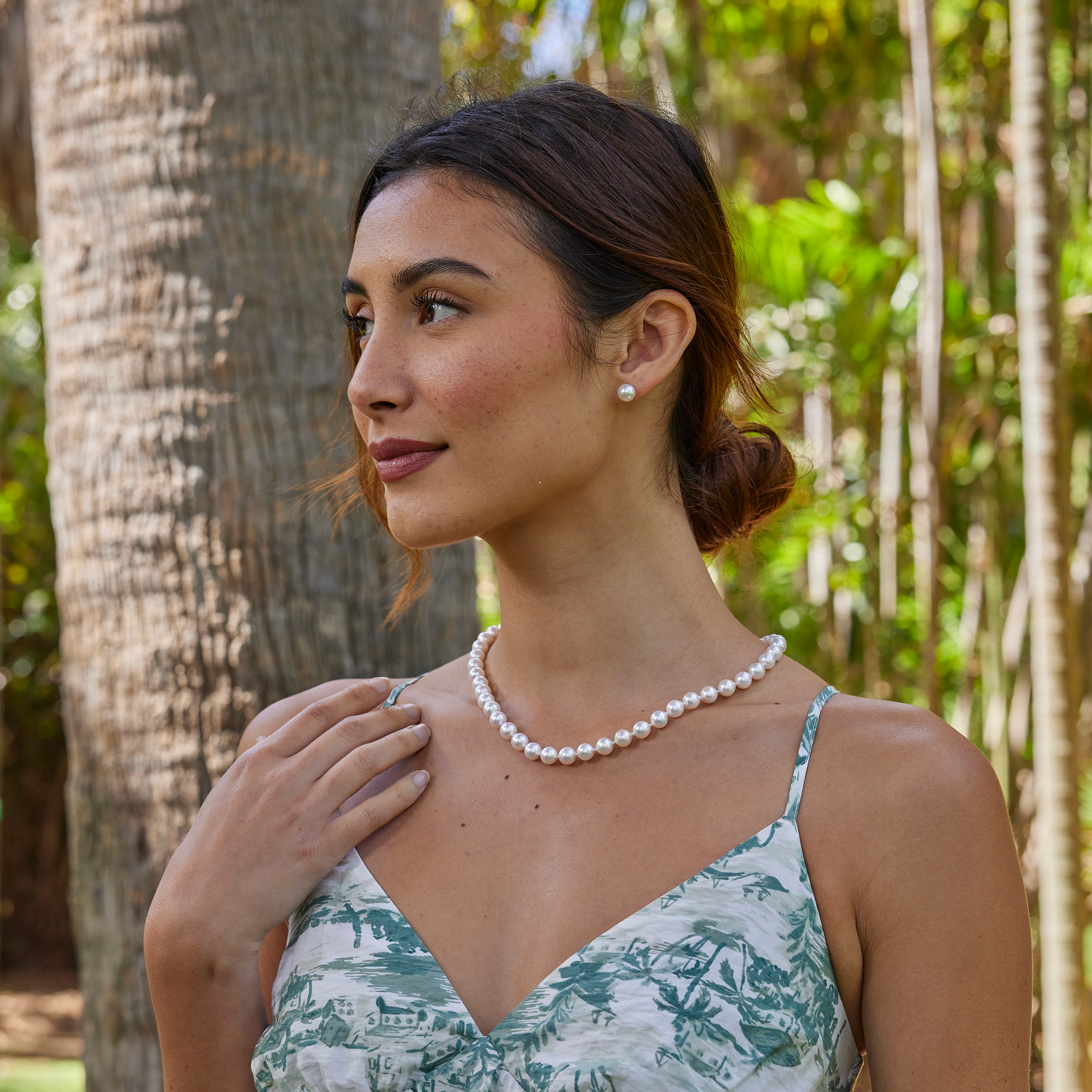 Woman wearing an Akoya white pearl strand necklace and matching pearl earrings against a blurred background