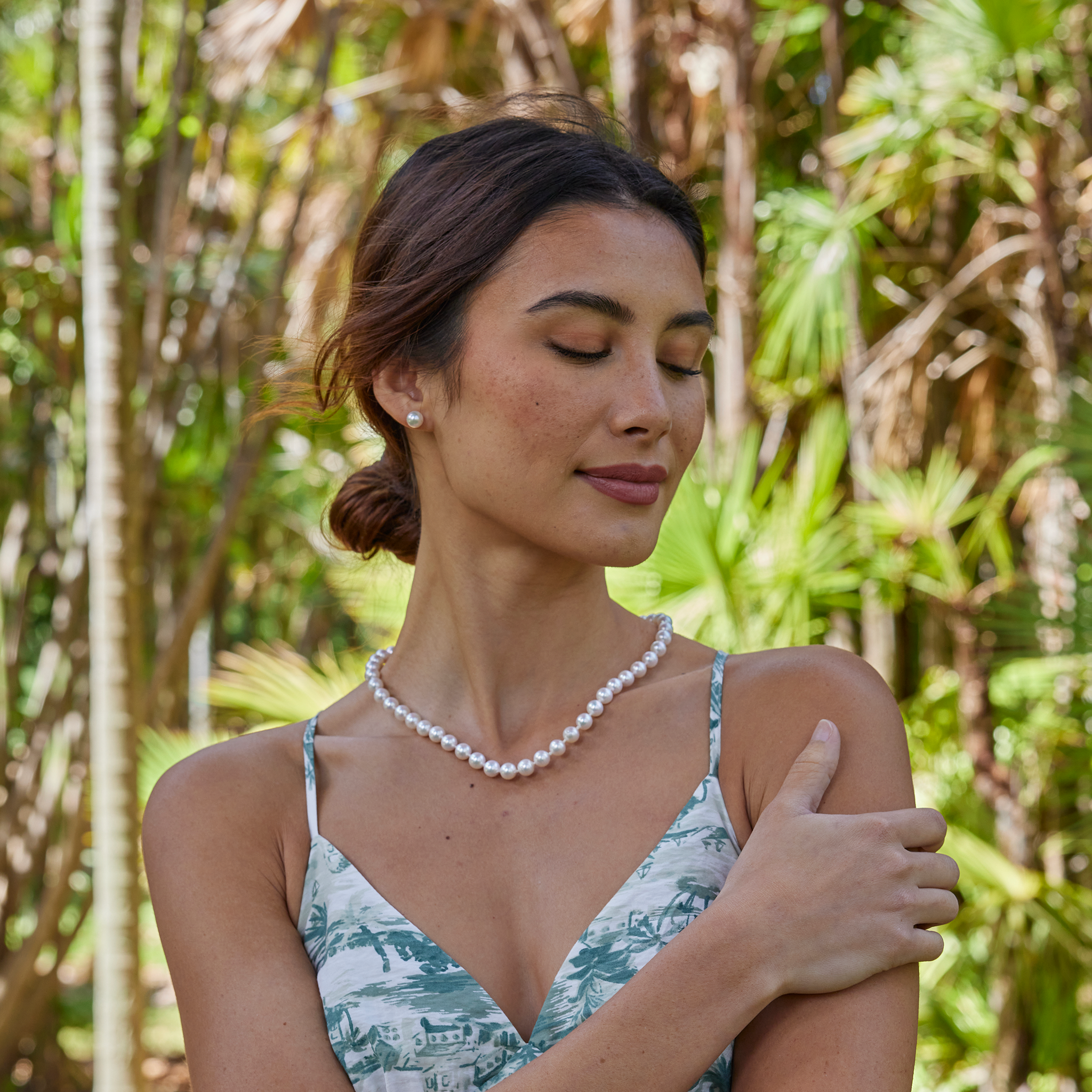 Woman wearing an Akoya white pearl strand necklace and matching pearl earrings against a blurred background