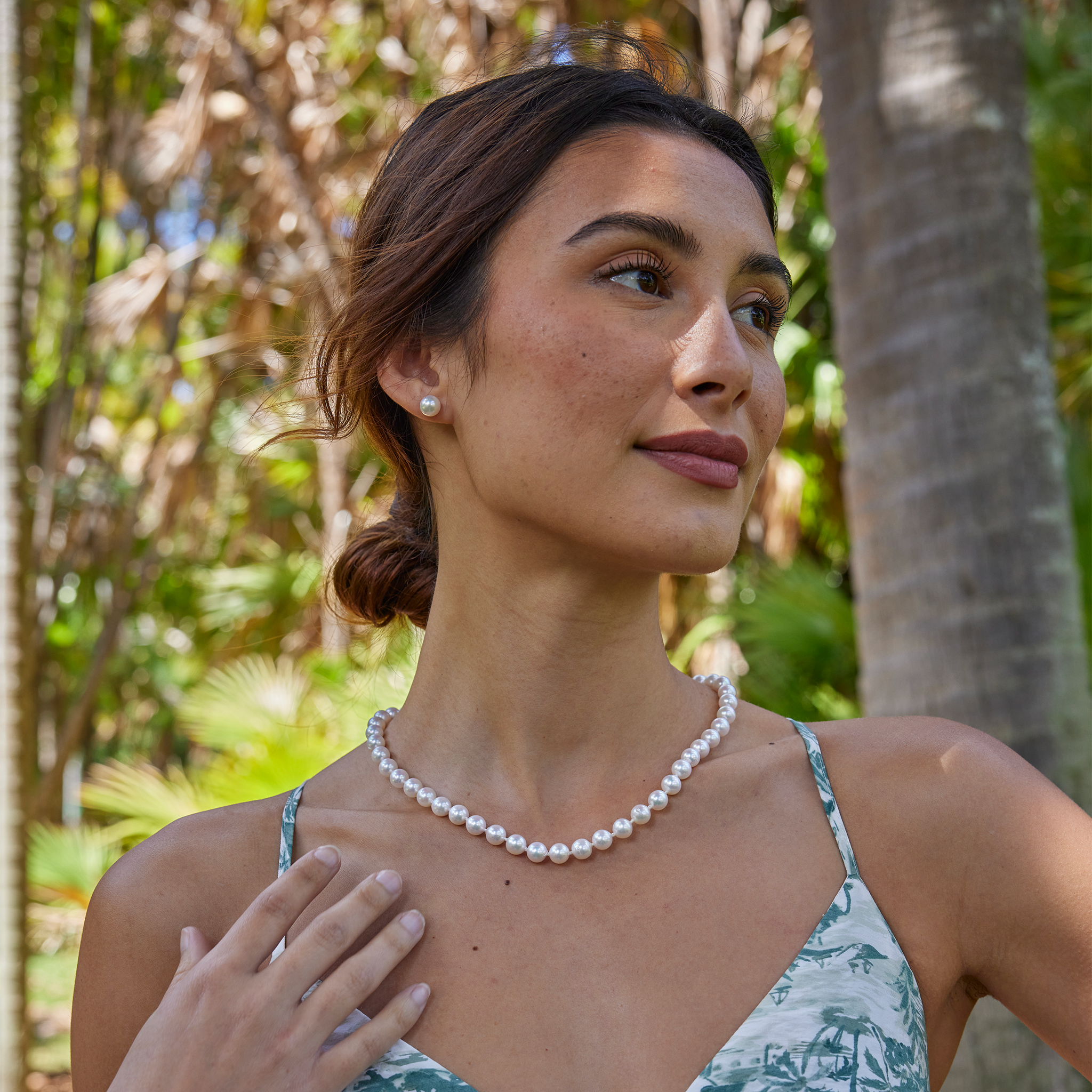 Woman wearing an Akoya white pearl strand necklace and matching pearl earrings against a blurred background
