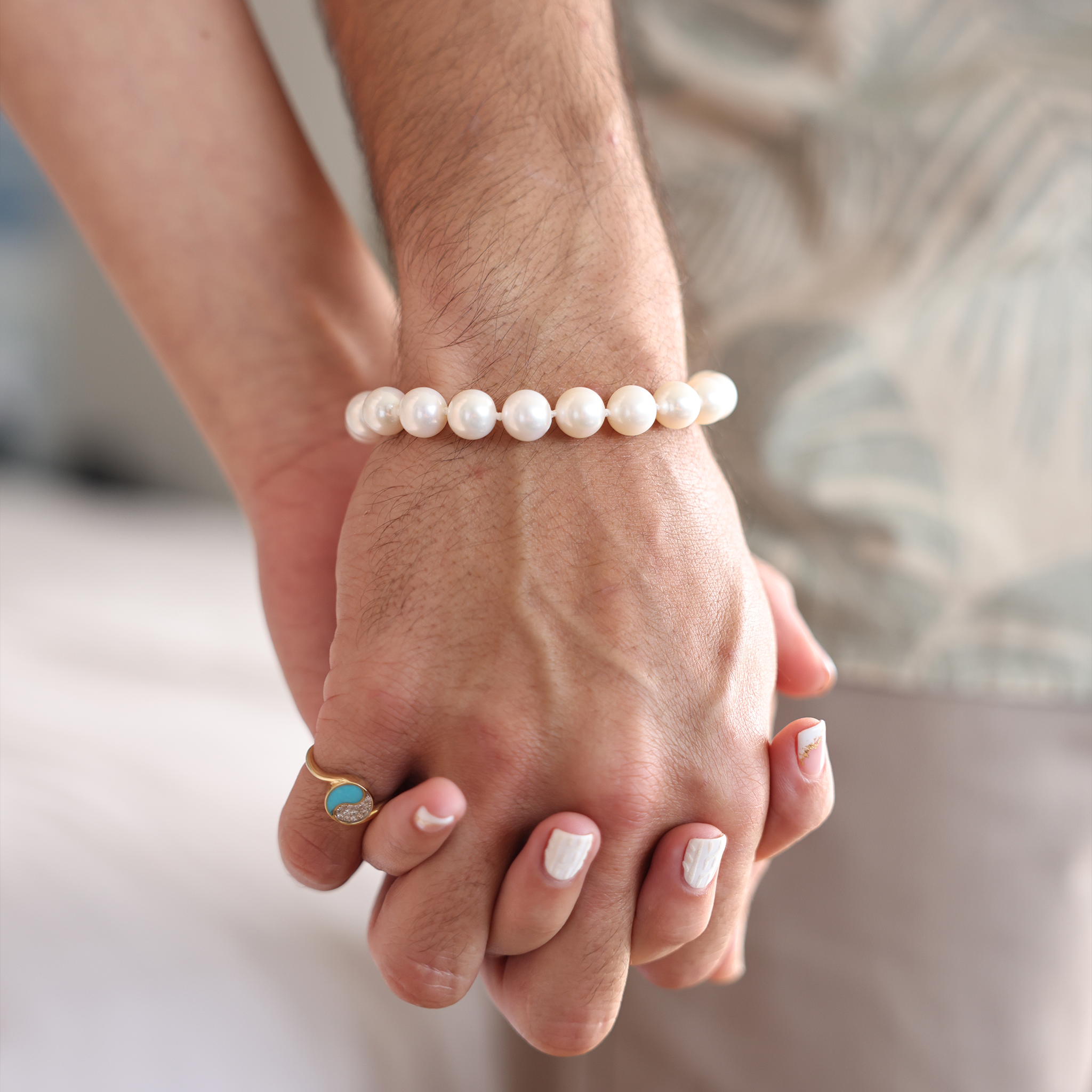 Close-up of two hands, one wearing a freshwater white pearl bracelet and a 14k gold ring set with turquoise and diamonds