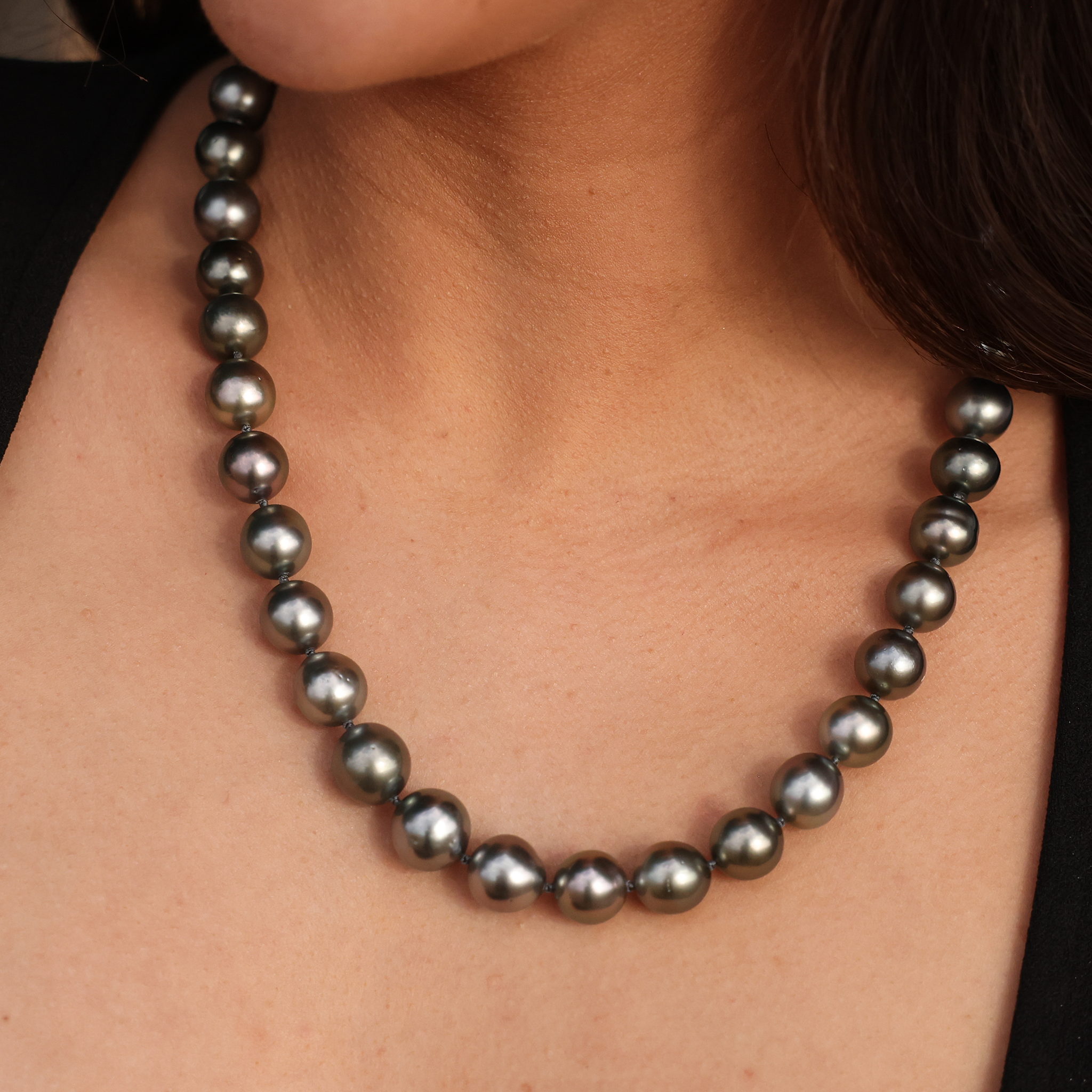 Macro close-up of a Tahitian black pearl strand necklace worn around a neck