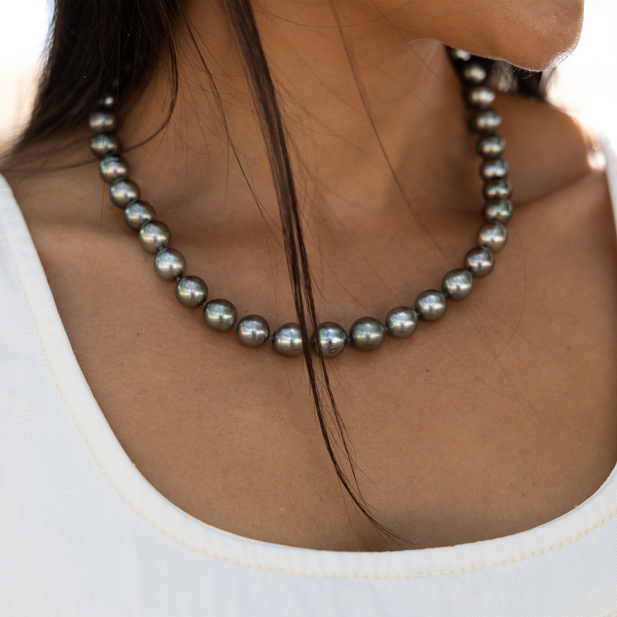 Close-up of a woman in a white shirt wearing a Tahitian black pearl strand necklace