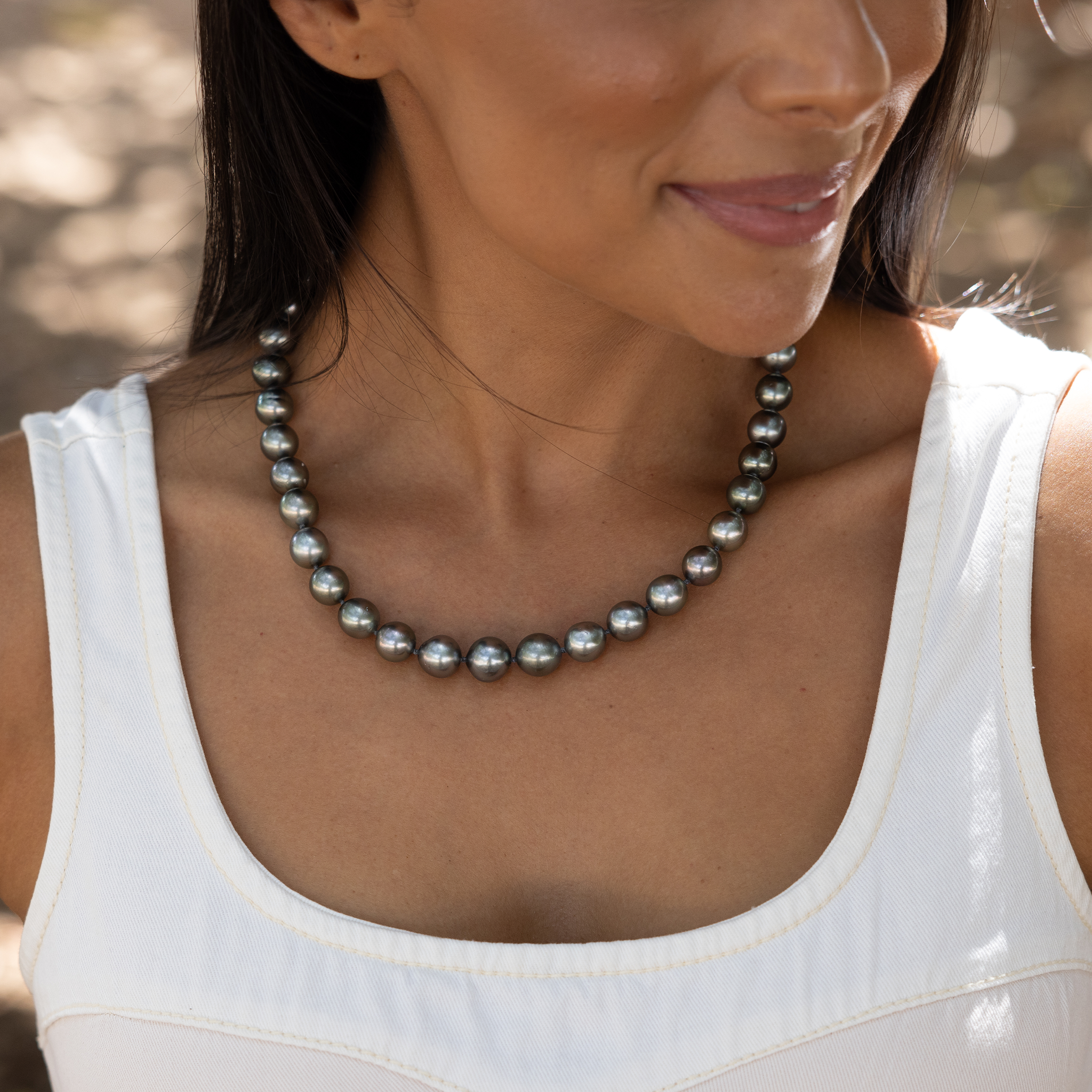 Close-up of a smiling woman in a white shirt wearing a Tahitian black pearl strand necklace
