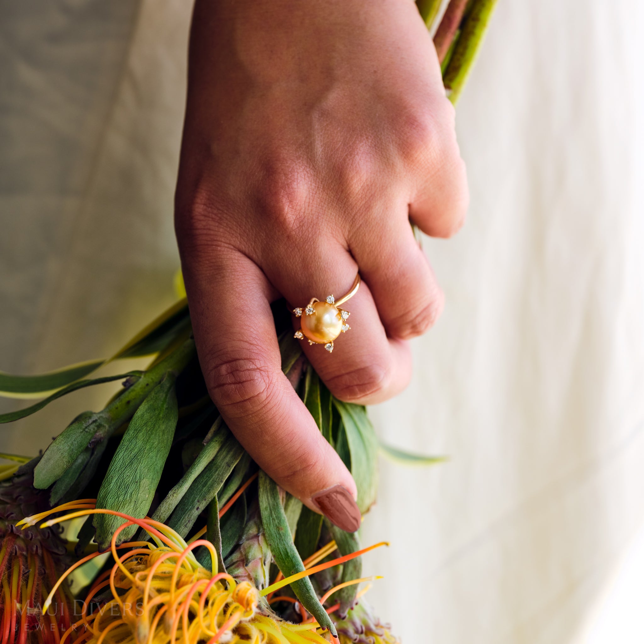 Close-up of a South Sea gold pearl ring with diamonds in 14k yellow gold worn on a hand holding a bouquet of flowers.