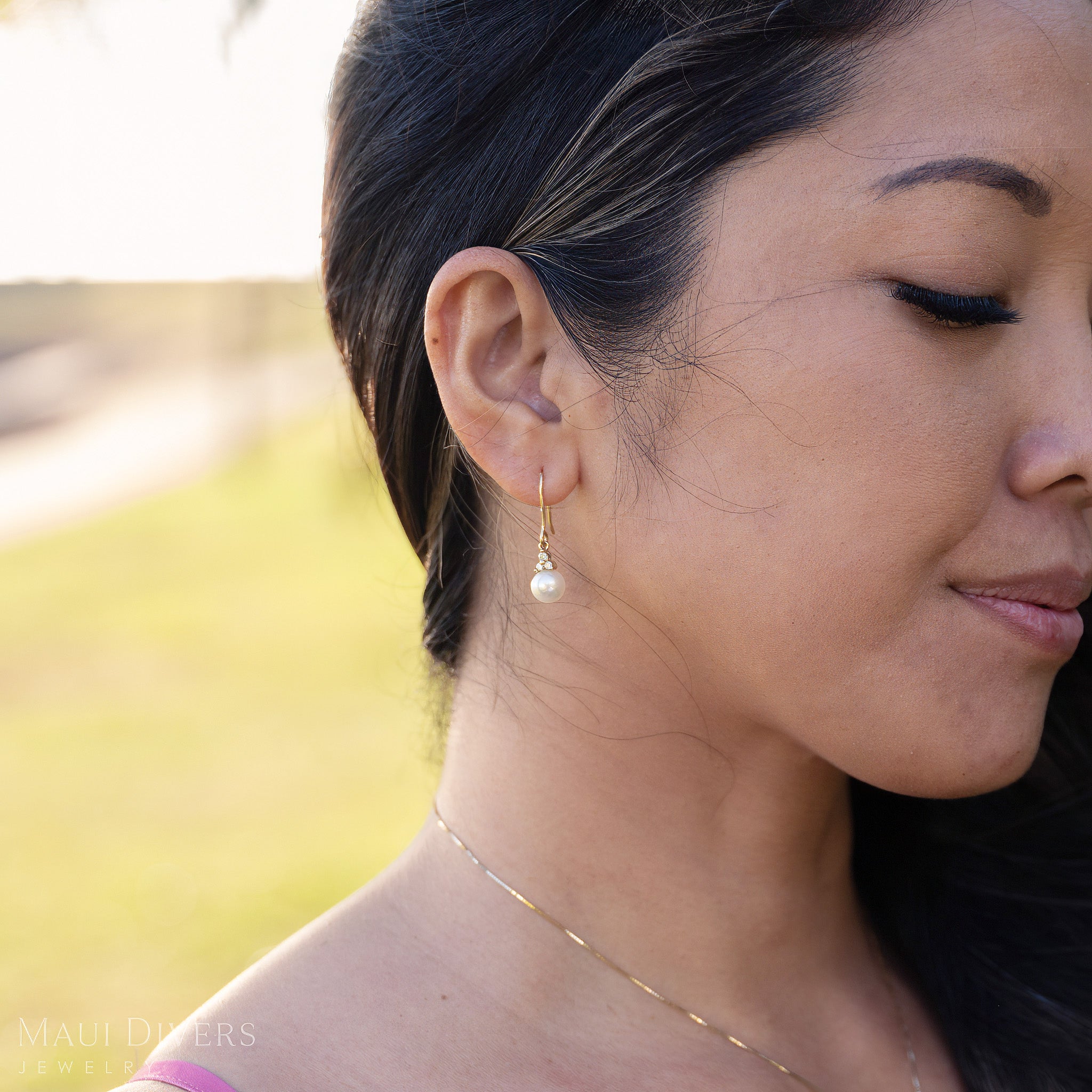 Close-up of a woman wearing diamond Akoya white earrings with a blurred natural background