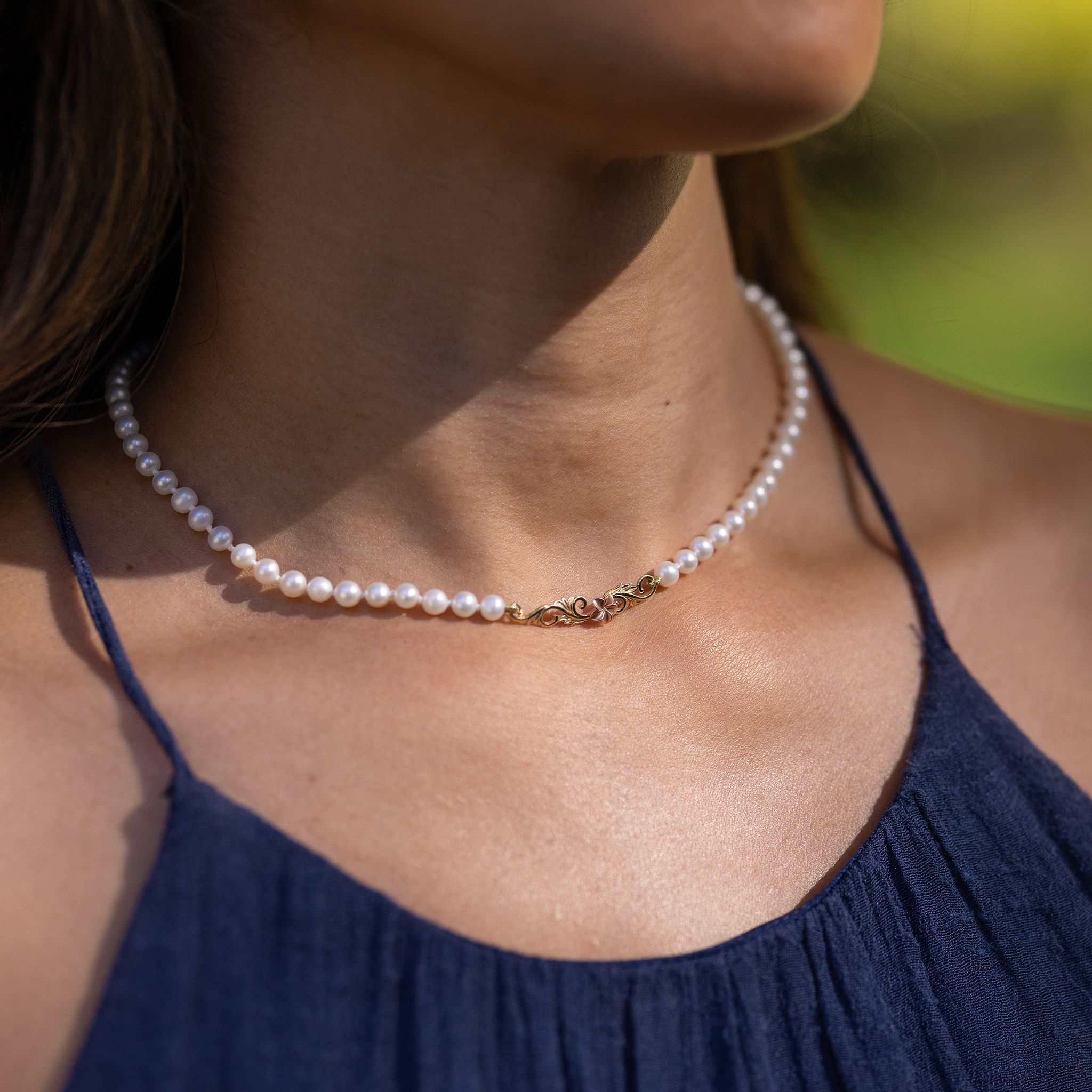 Close up of a woman wearing the Hawaiian Heirloom Plumeria Freshwater White Pearl Necklace