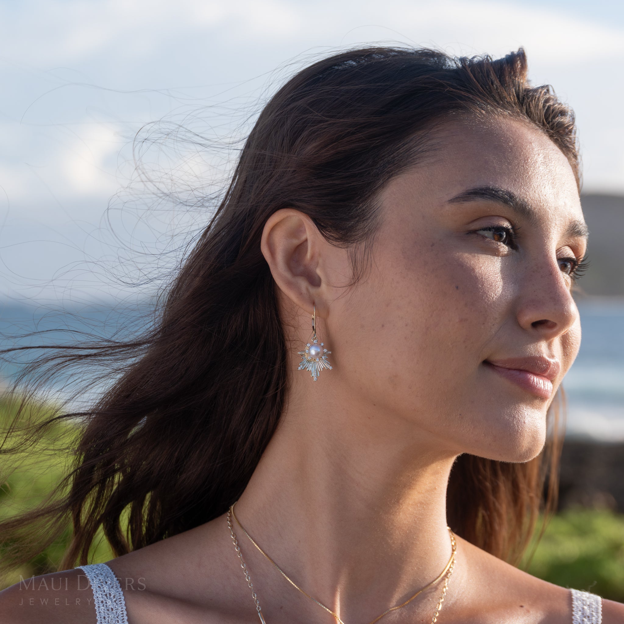 Woman wearing E Hoʻāla Akoya White Pearl Earrings in yellow gold with diamonds, with a scenic background