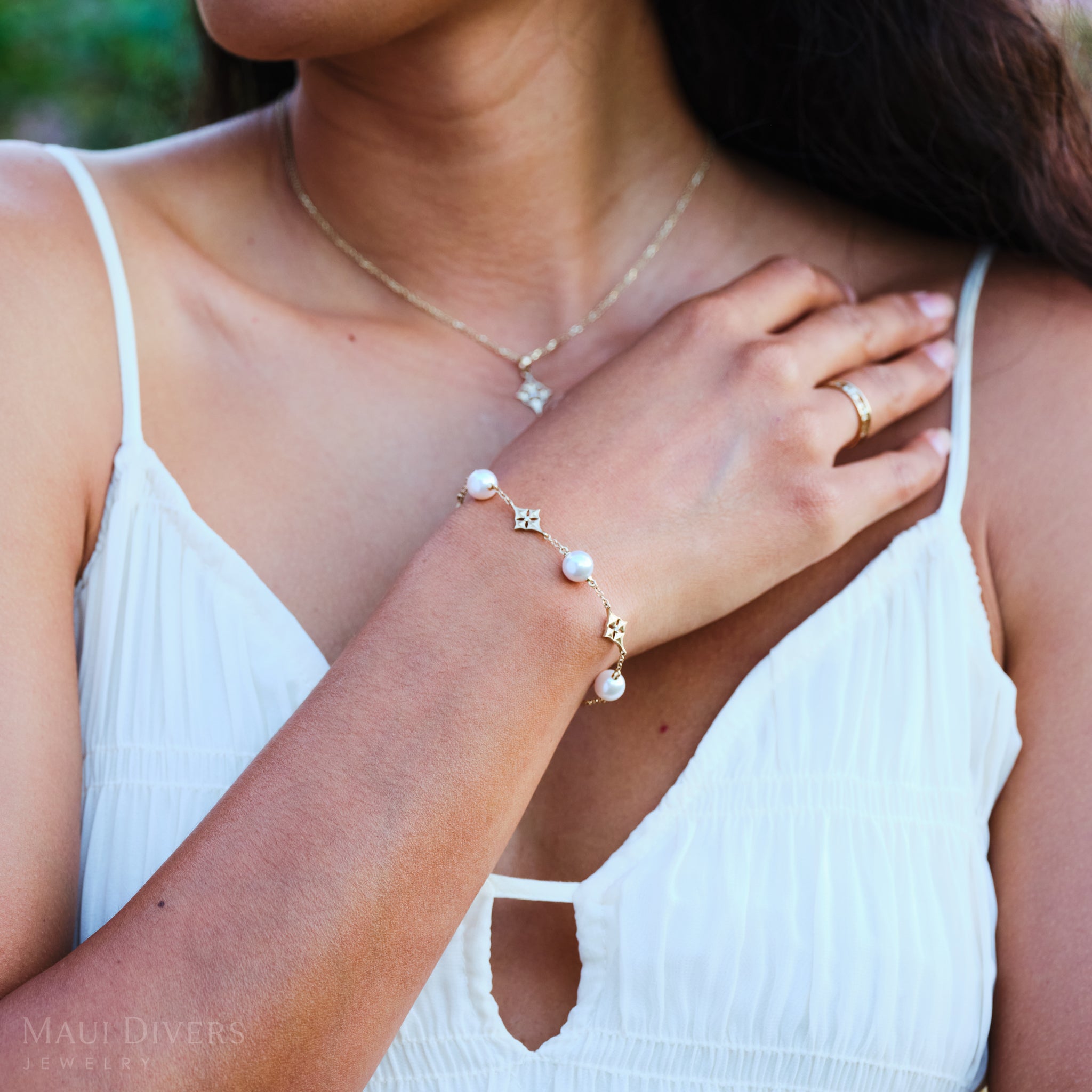 Woman wearing a Hawaiian Quilted Star Akoya White Pearl Bracelet in Gold with Diamonds, with a blurred background