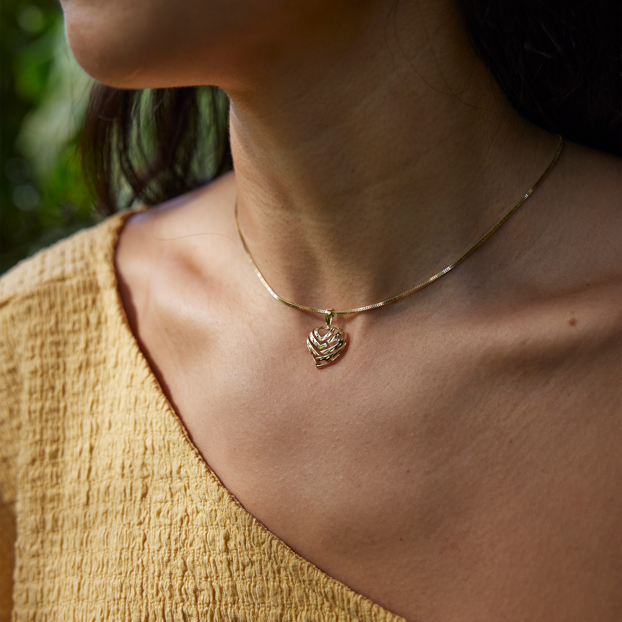Close-up of a person wearing an Aloha Heart Pendant with cut-out design spelling "Aloha" in 14k Yellow Gold on chain