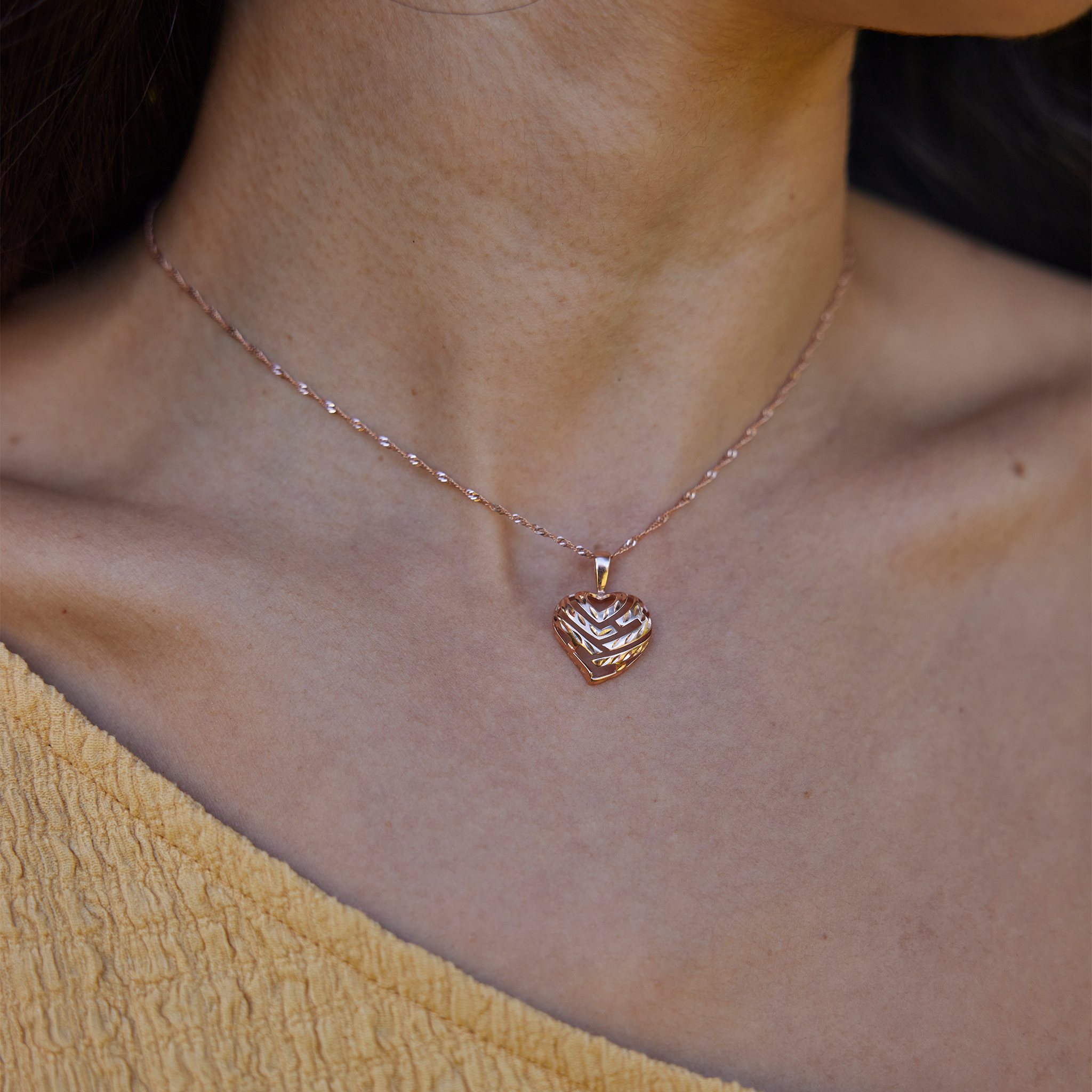 Close-up of a person wearing an Aloha Heart Pendant with cut-out design spelling "Aloha" in 14k Rose Gold on chain
