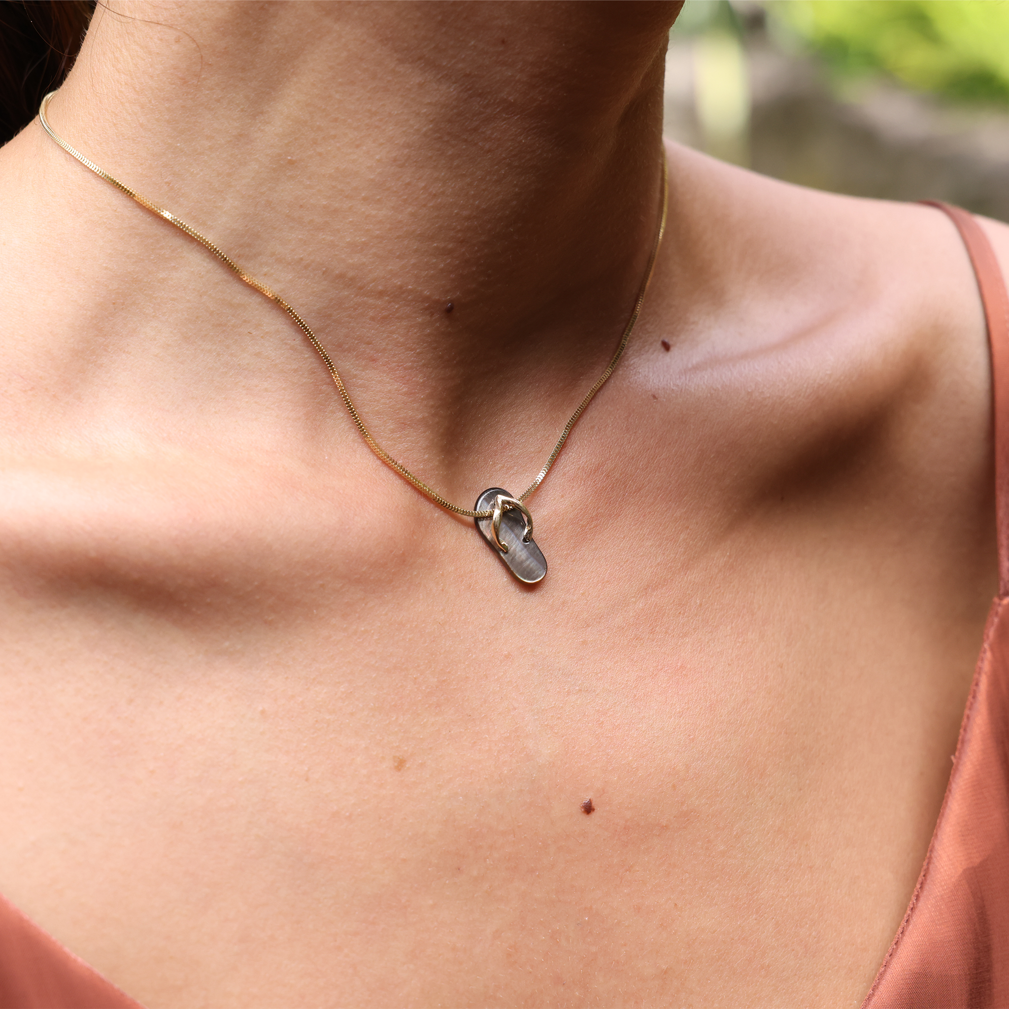 Close-up of a neckline with a Black Mother of Pearl Slipper Pendant hanging on a Yellow Gold Chain