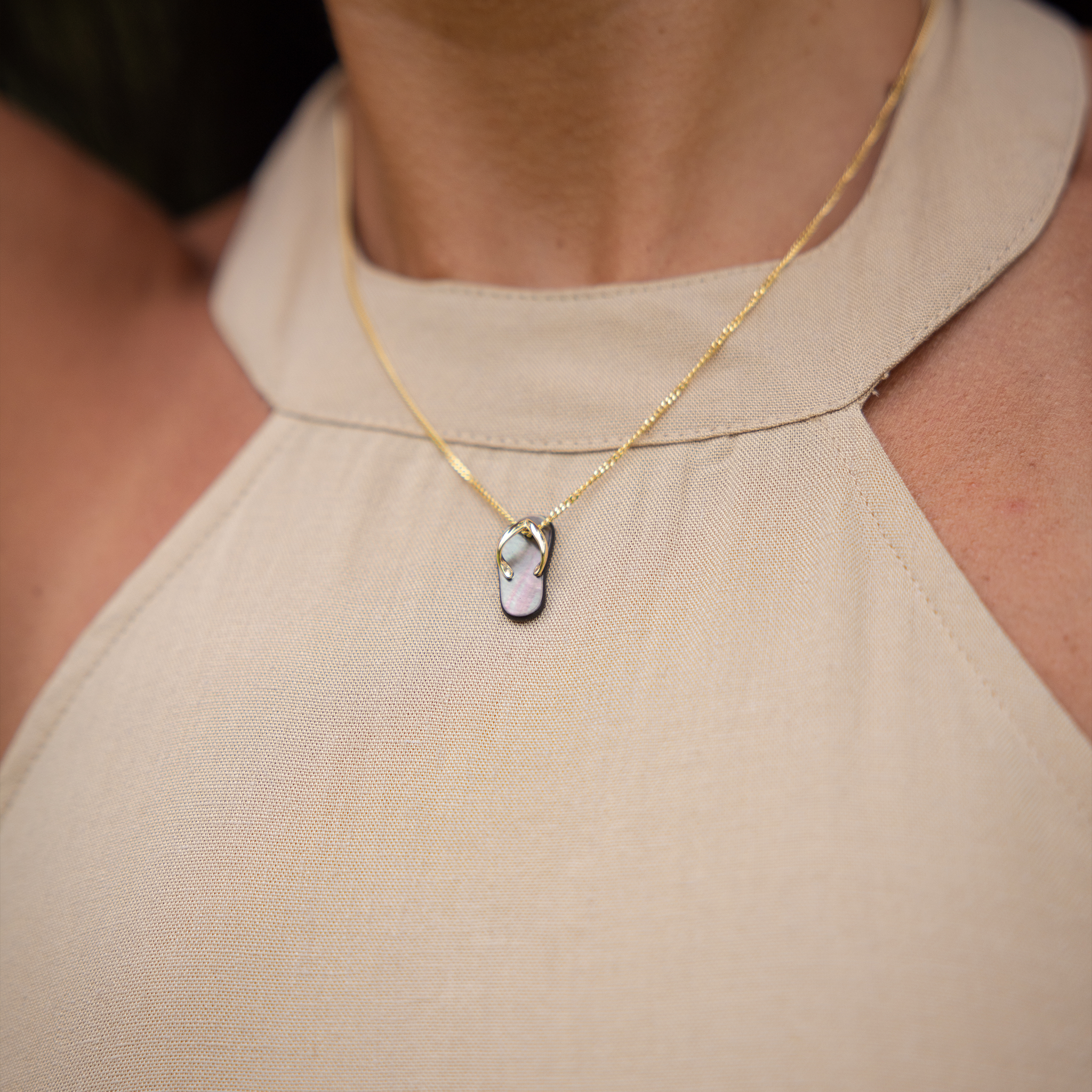 Close-up of a neckline with a Black Mother of Pearl Slipper Pendant hanging on a Yellow Gold Chain