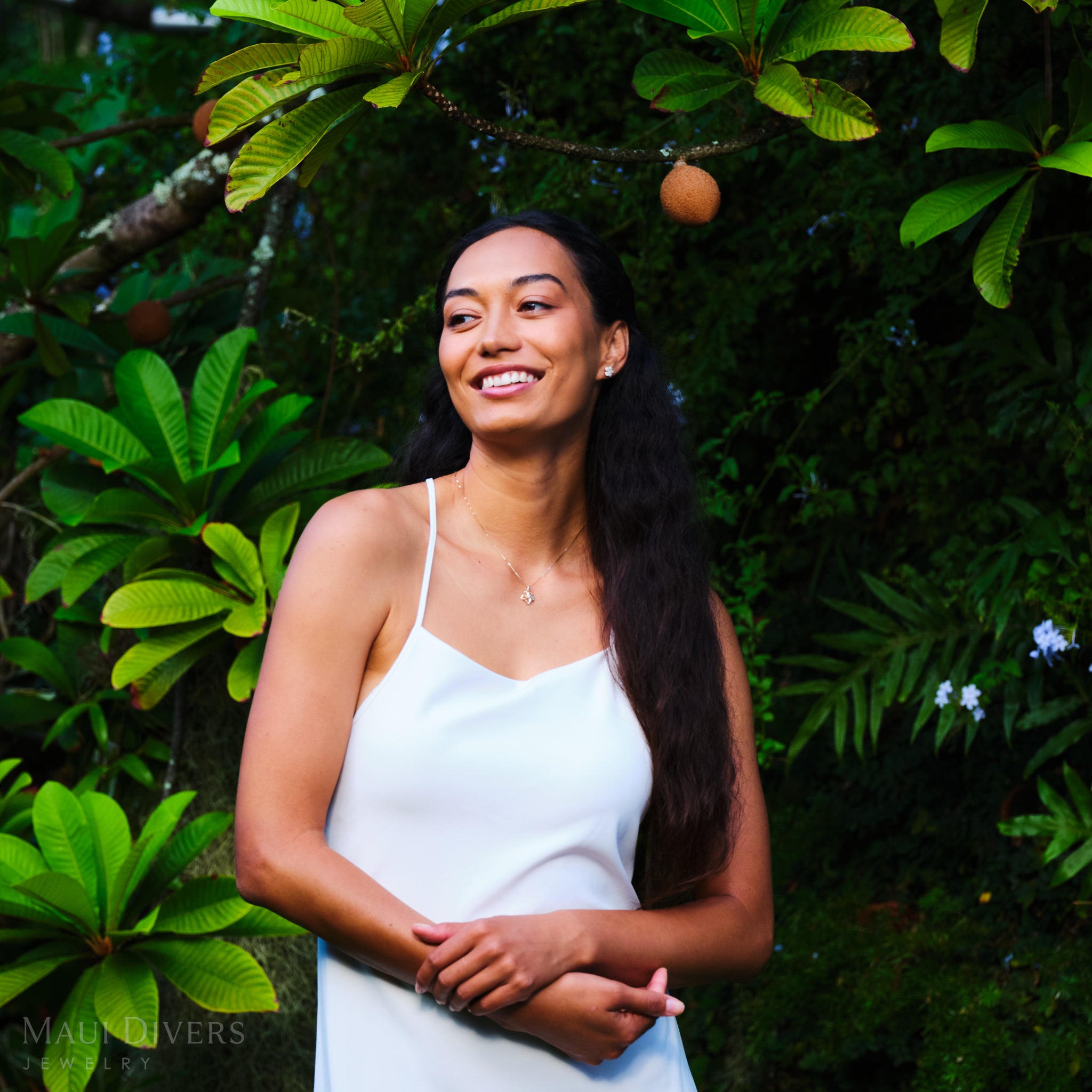 Woman in a white dress standing in a lush green garden wearing a Yellow Gold Plumeria Necklace