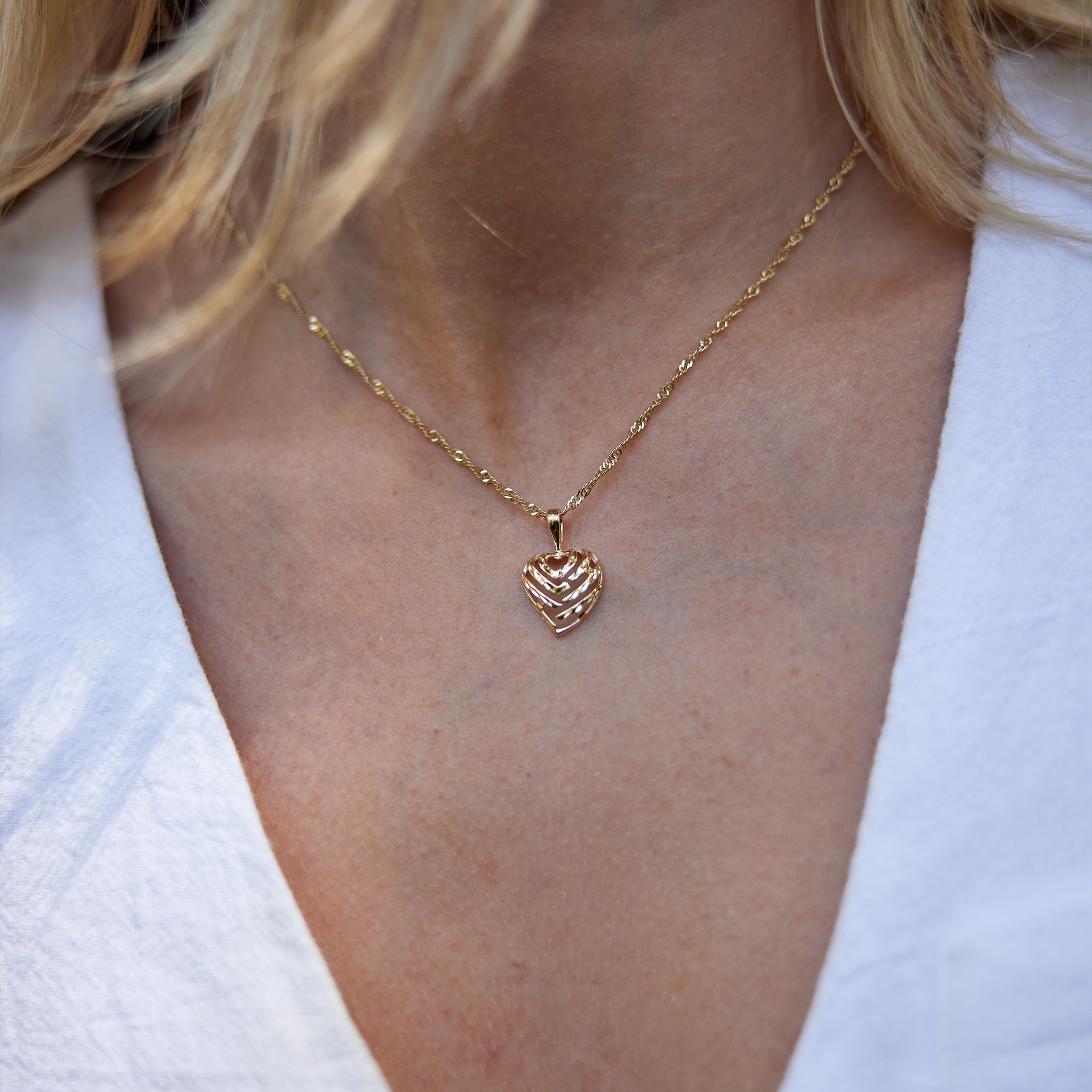 Close up of woman's neckline wearing Gold Aloha Heart Pendant with cut-out design spelling "Aloha"