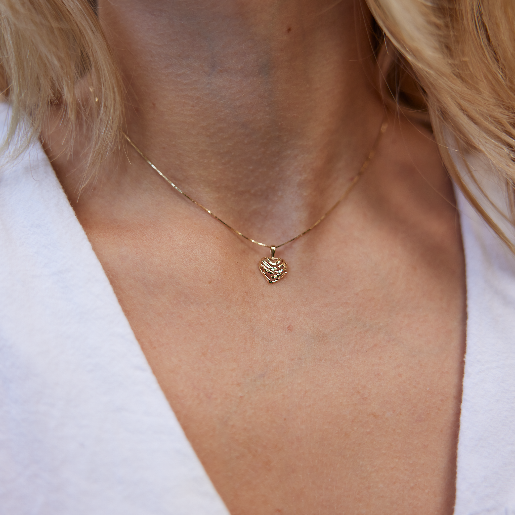 Close up of woman's neckline wearing cut -out Aloha Heart Pendant in Gold on box chain