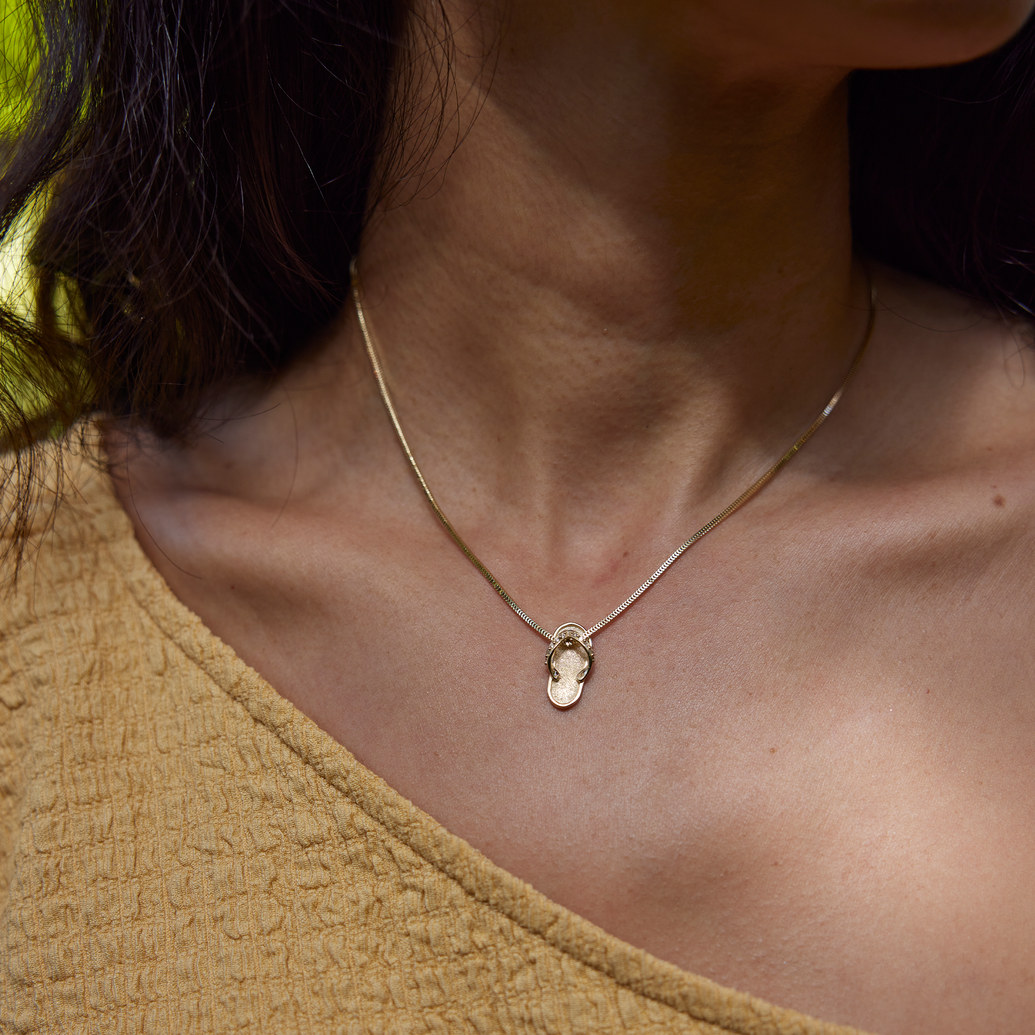 Neckline of woman wearing yellow gold slipper pendant with diamond straps on chain