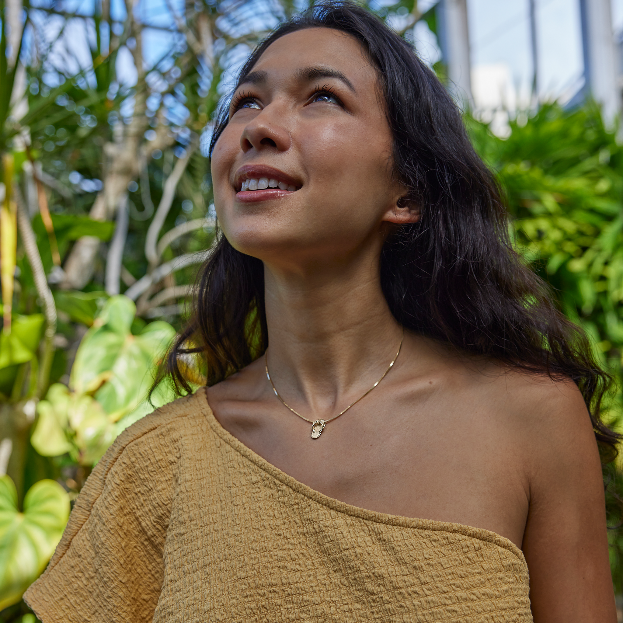 Smiling woman in lush garden wearing gold slipper pendant on chain