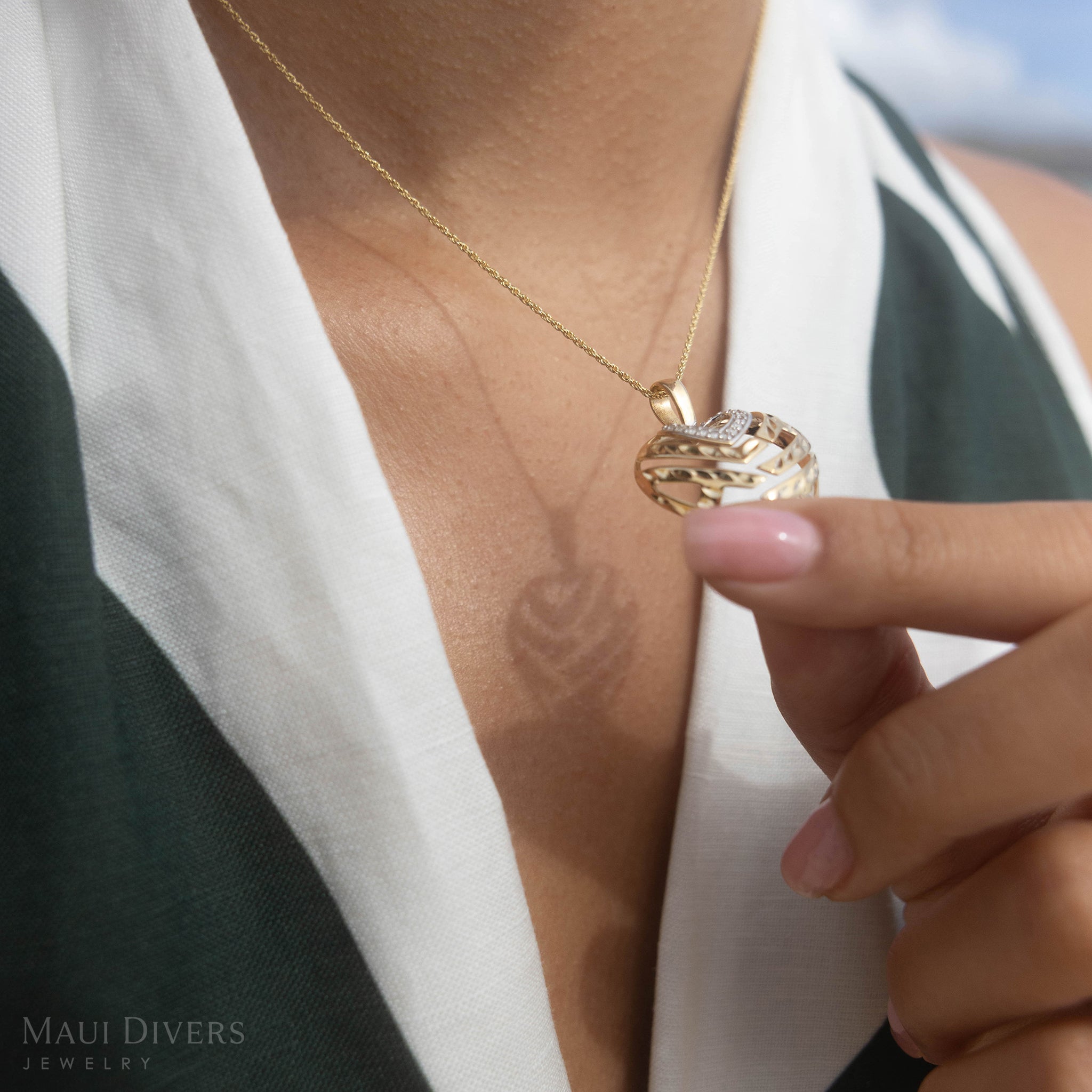 Gold Aloha Heart necklace with a pendant held by a hand casting a shadow that spells Aloha