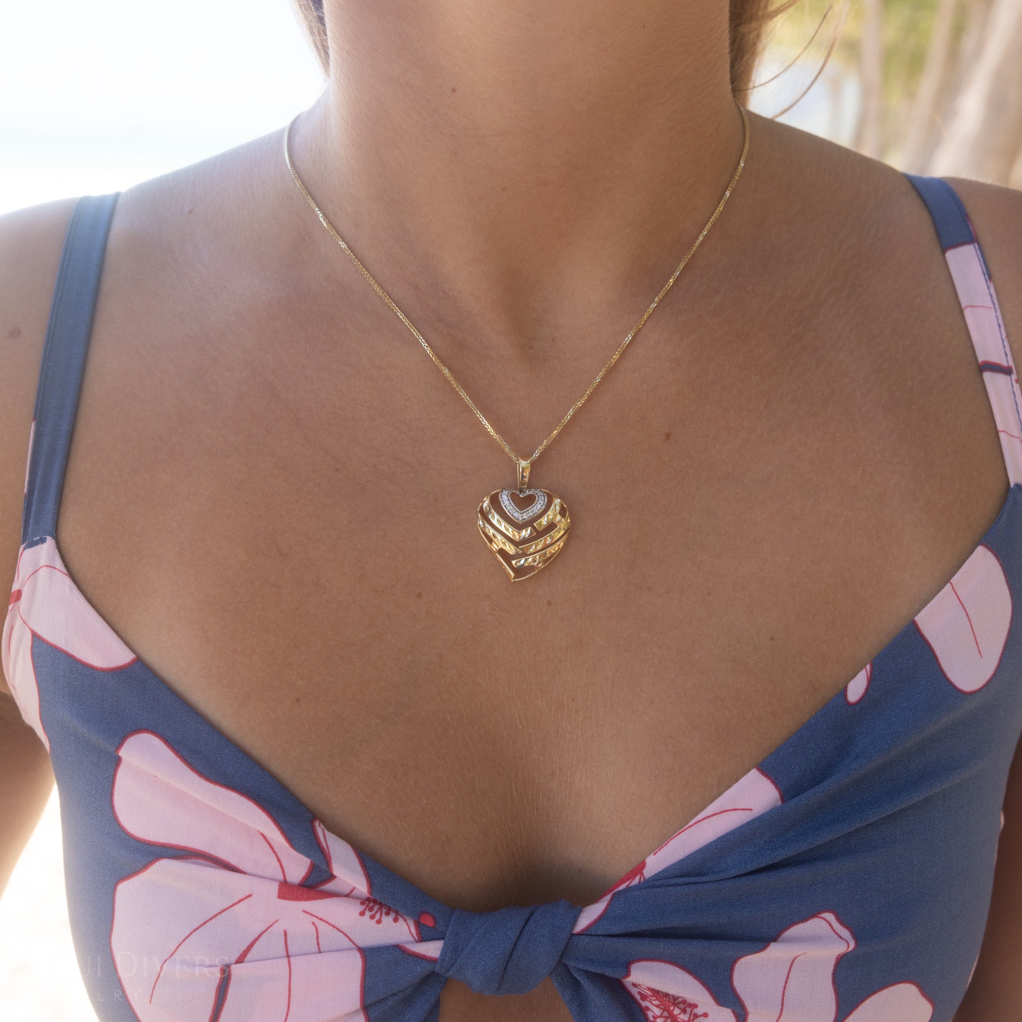 Woman wearing a two-tone gold heart-shaped pendant necklace with a floral top.