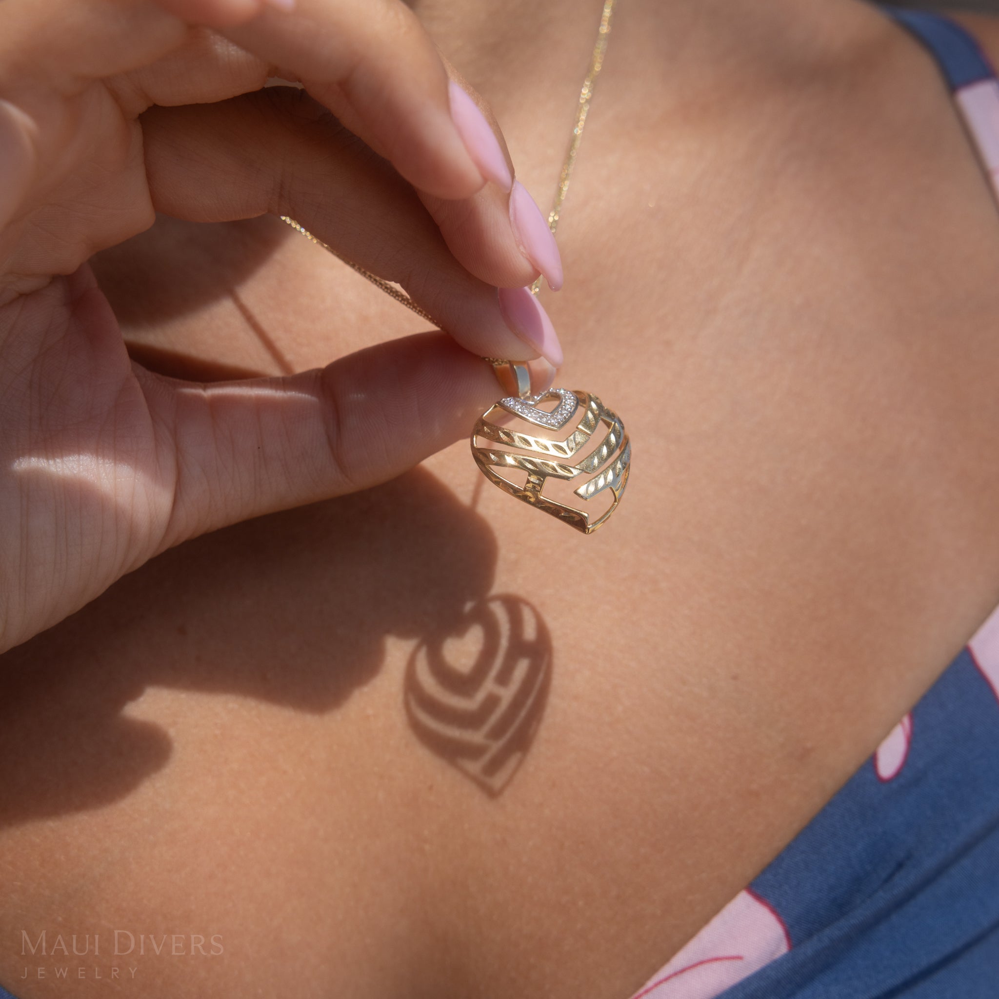 Detailed shot of woman holding an Aloha Heart Pendant casting a shadow that spells Aloha