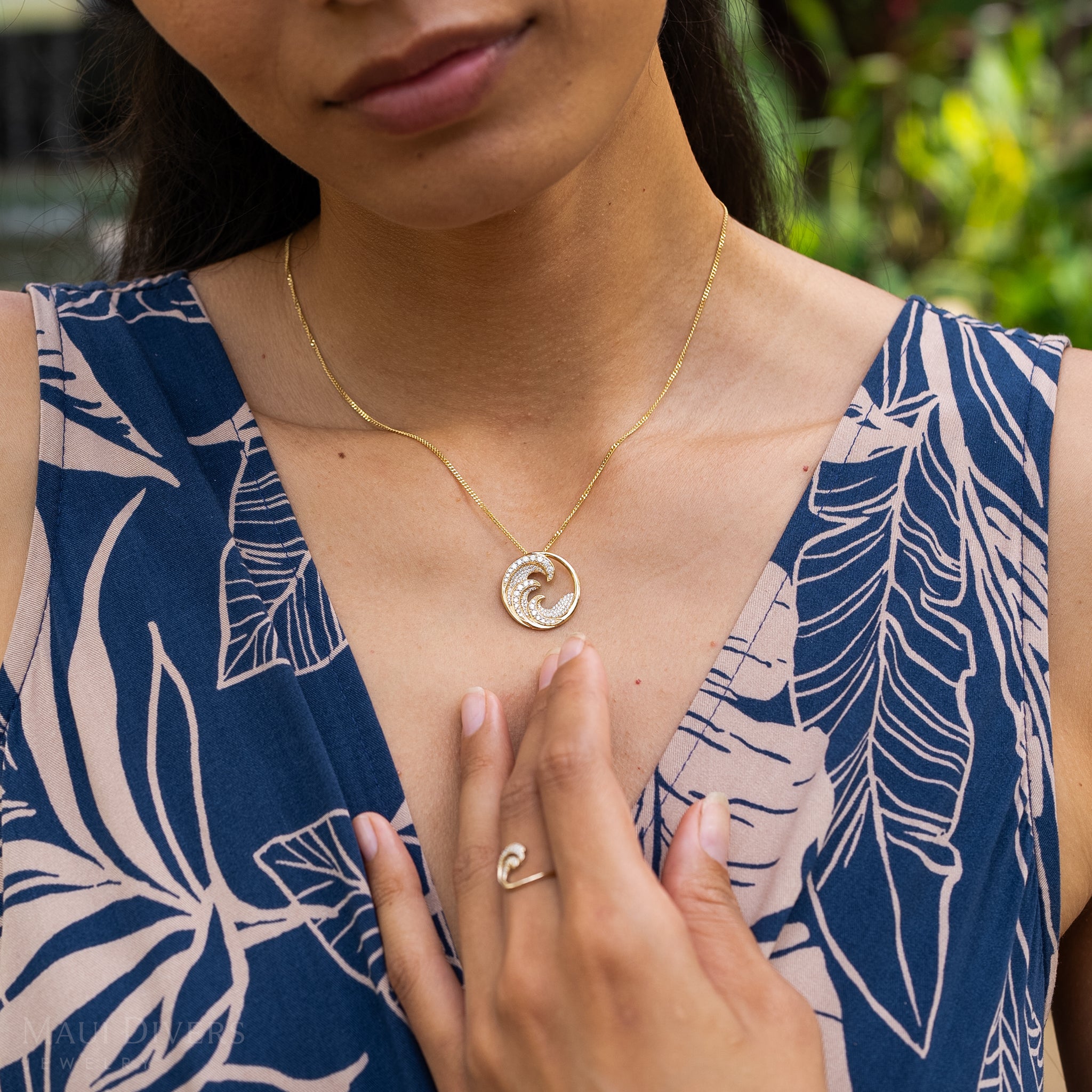 Close up of a woman wearing a diamond encrusted triple wave pendant in gold with matching ring