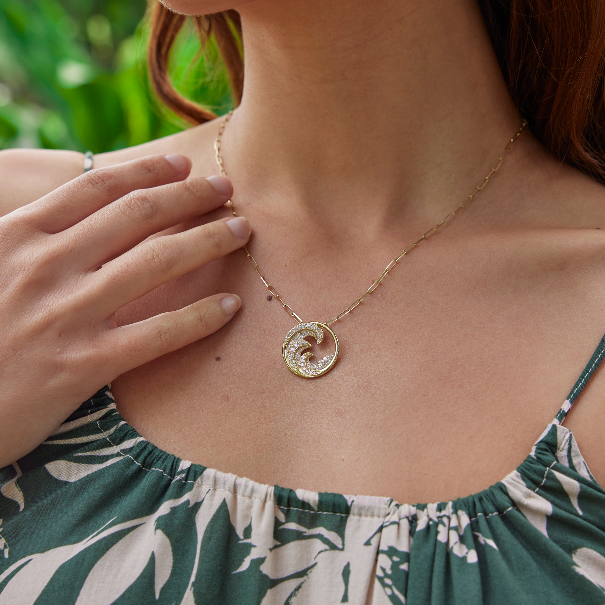 Close up of woman wearing diamond encrusted triple wave pendant in gold on paper clip chain