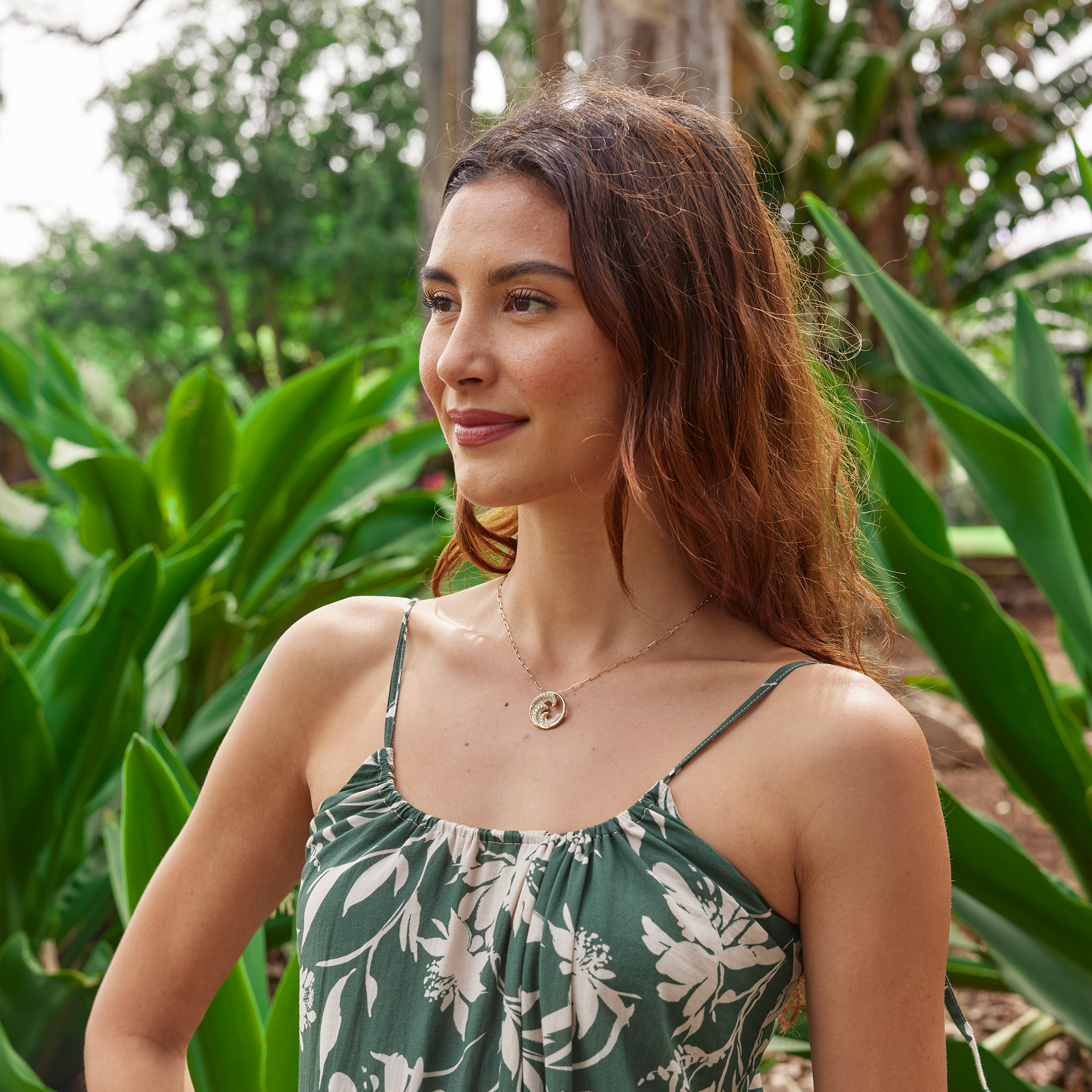 Woman in a lush garden wearing a diamond encrusted triple wave pendant in gold on paper clip chain