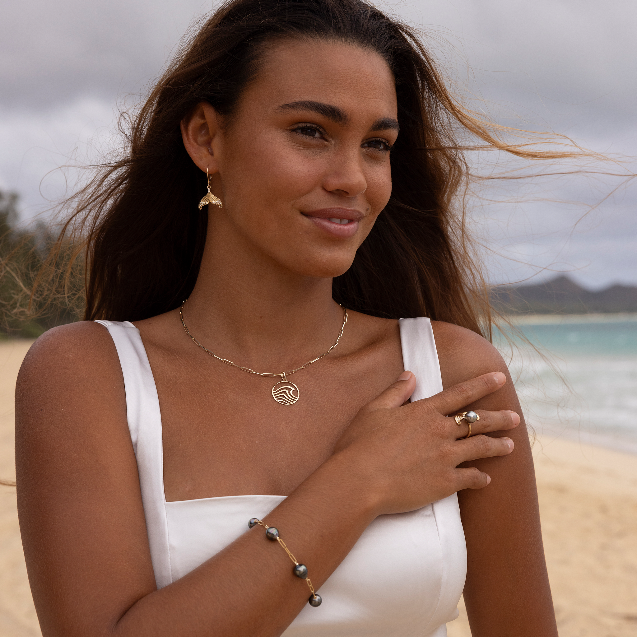 Woman on a beach wearing a white dress with a wave necklace on a paperclip chain