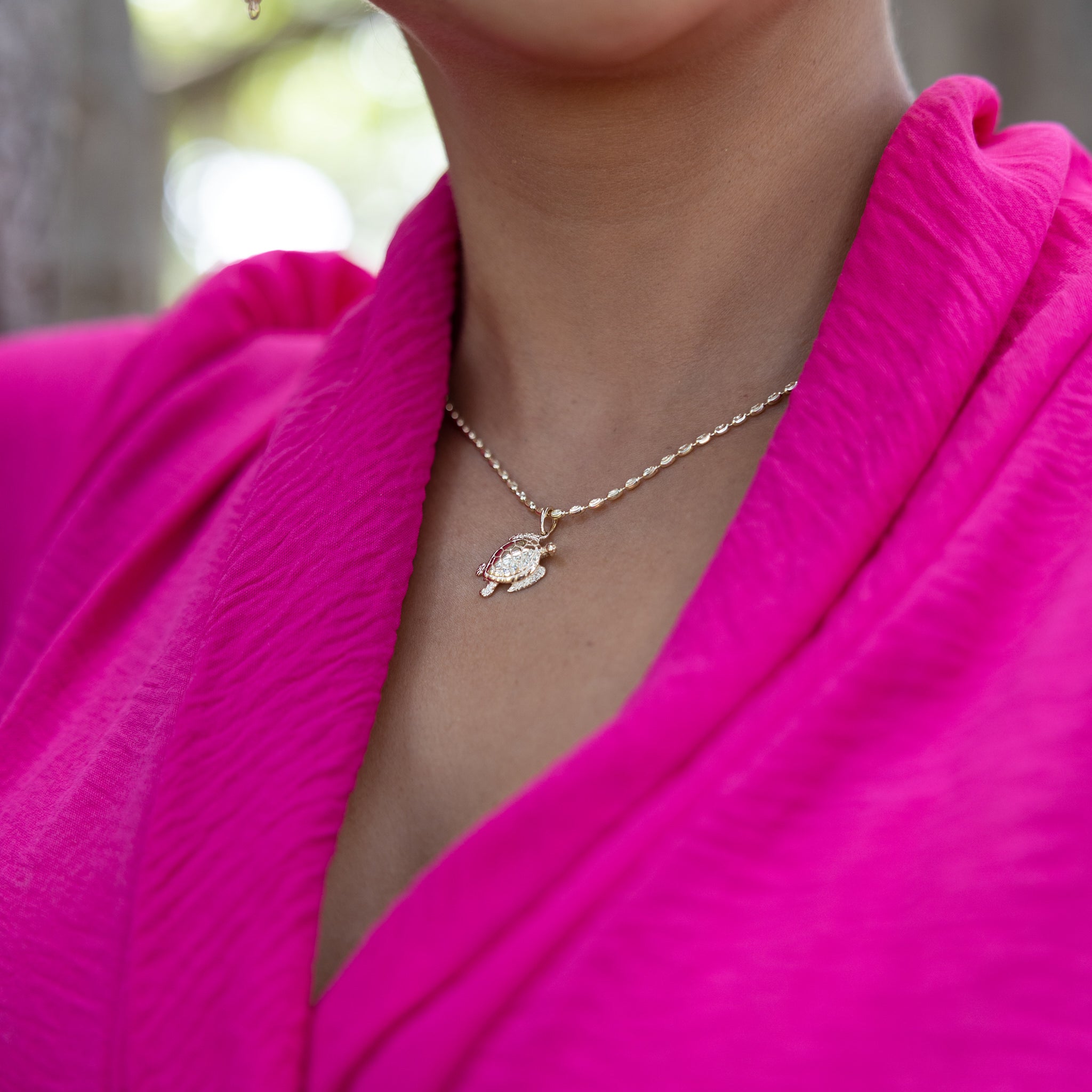 A woman wearing a 1.8mm Ovalina Chain in Gold with a turtle pendant and pink top outdoors