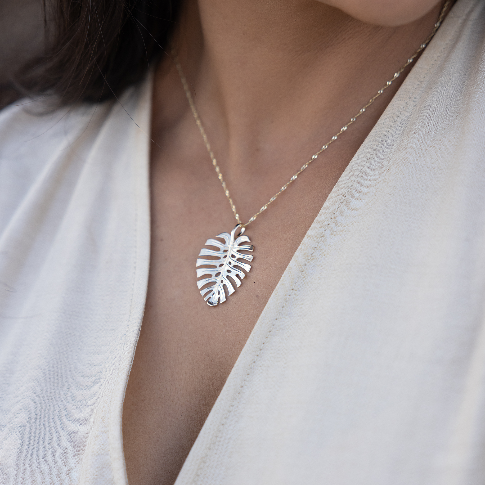 Close up of woman wearing gold monstera leaf pendant with high polish finish