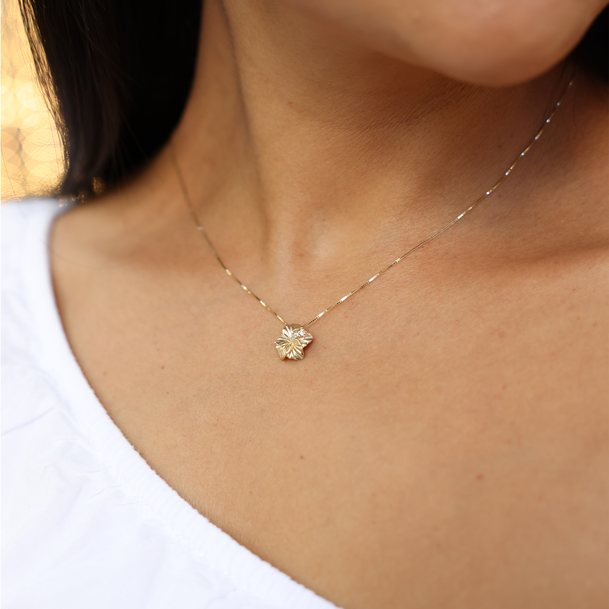 Person wearing the diamond hibiscus pendant in yellow gold on a box chain