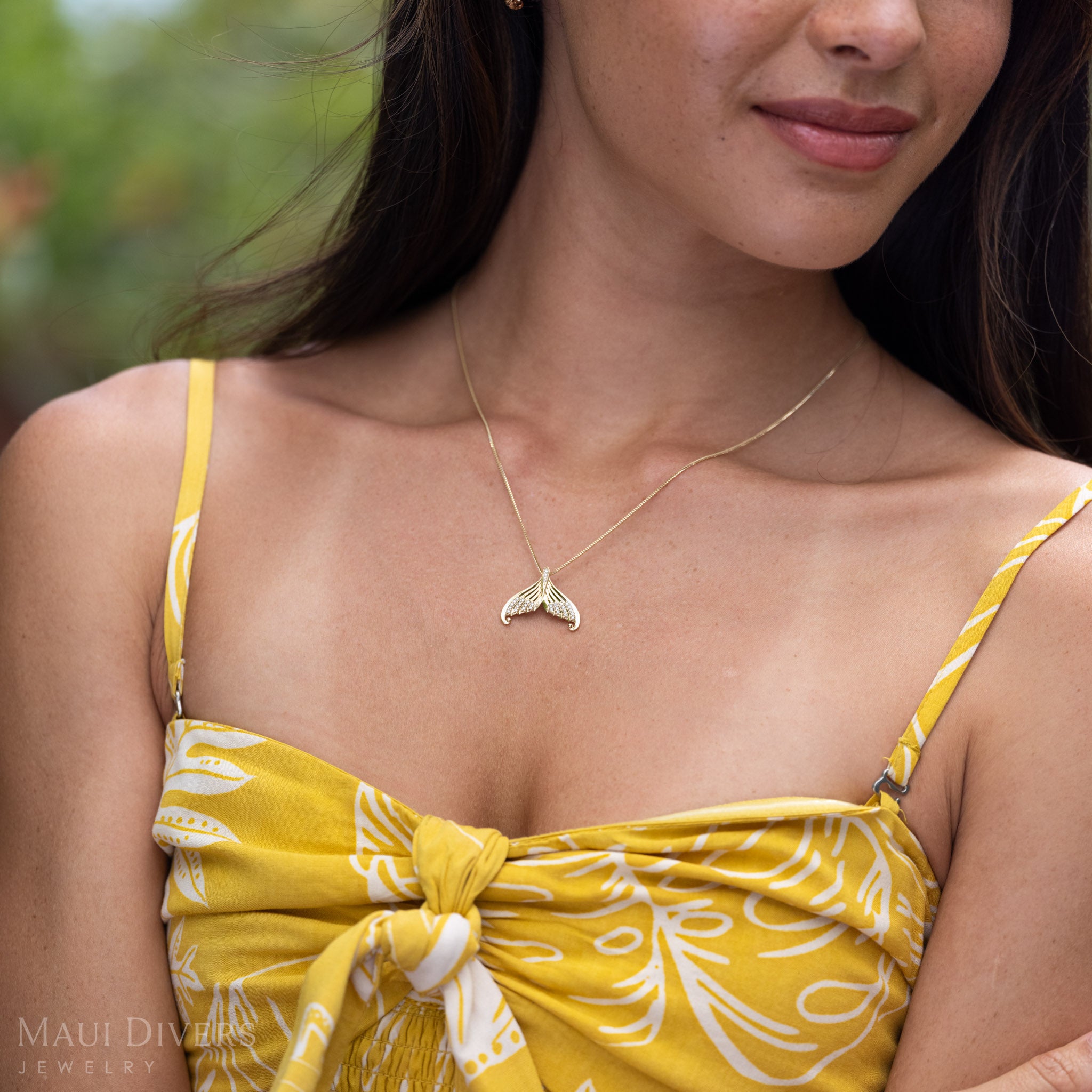Close-up of a woman wearing a Yellow Gold Mermaid Tail Necklace with Natural Diamond accents on a box chain and a yellow patterned top