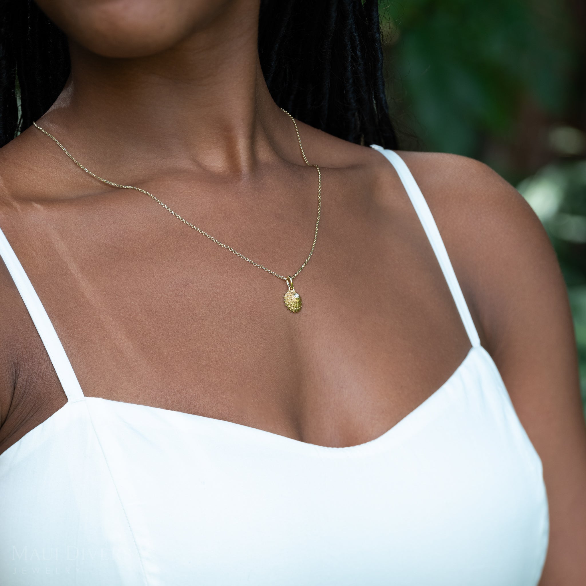 Woman wearing a 14k yellow gold necklace with an ʻOpihi diamond pendant against a blurred natural background