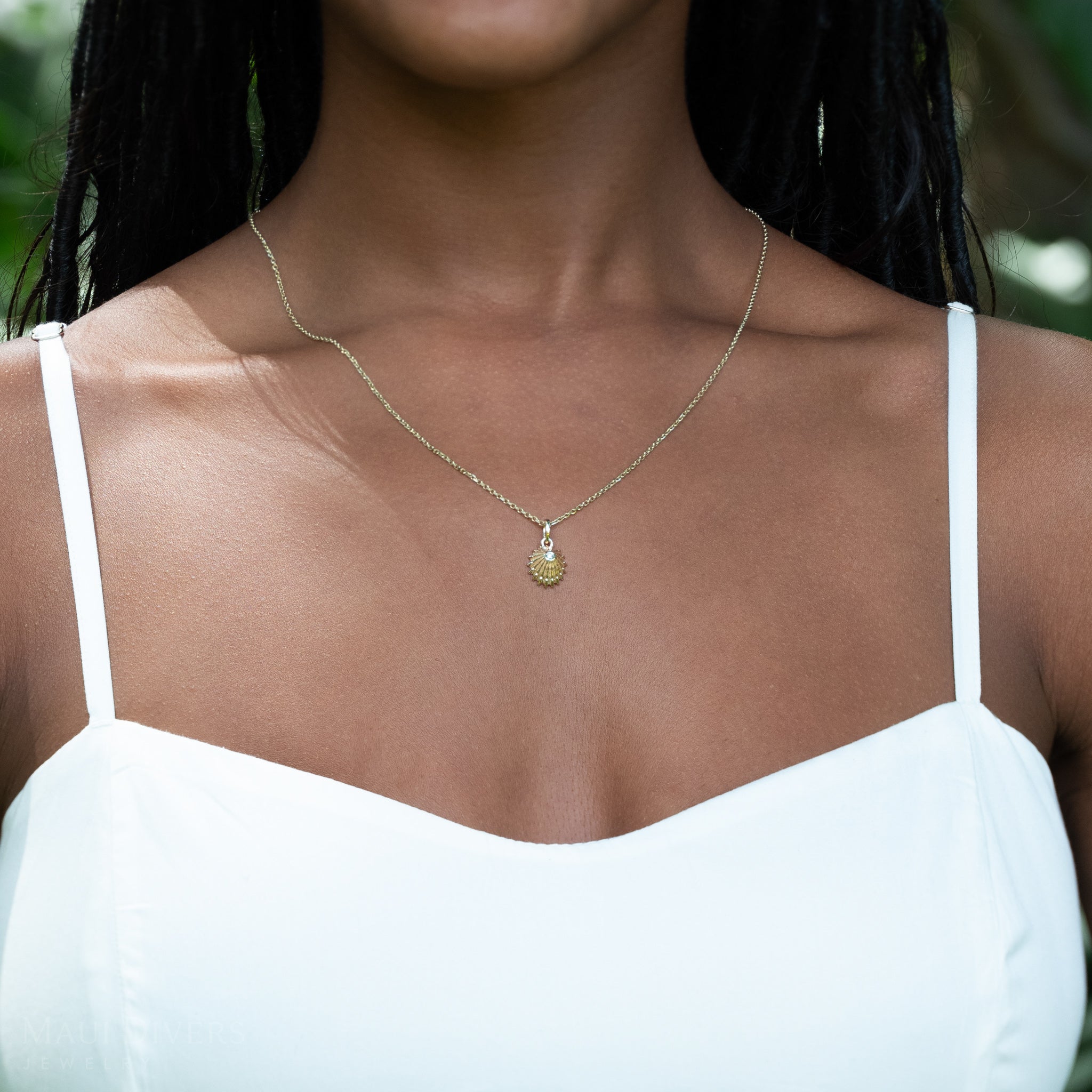 Woman wearing a gold necklace with an ʻOpihi diamond pendant against a blurred natural background