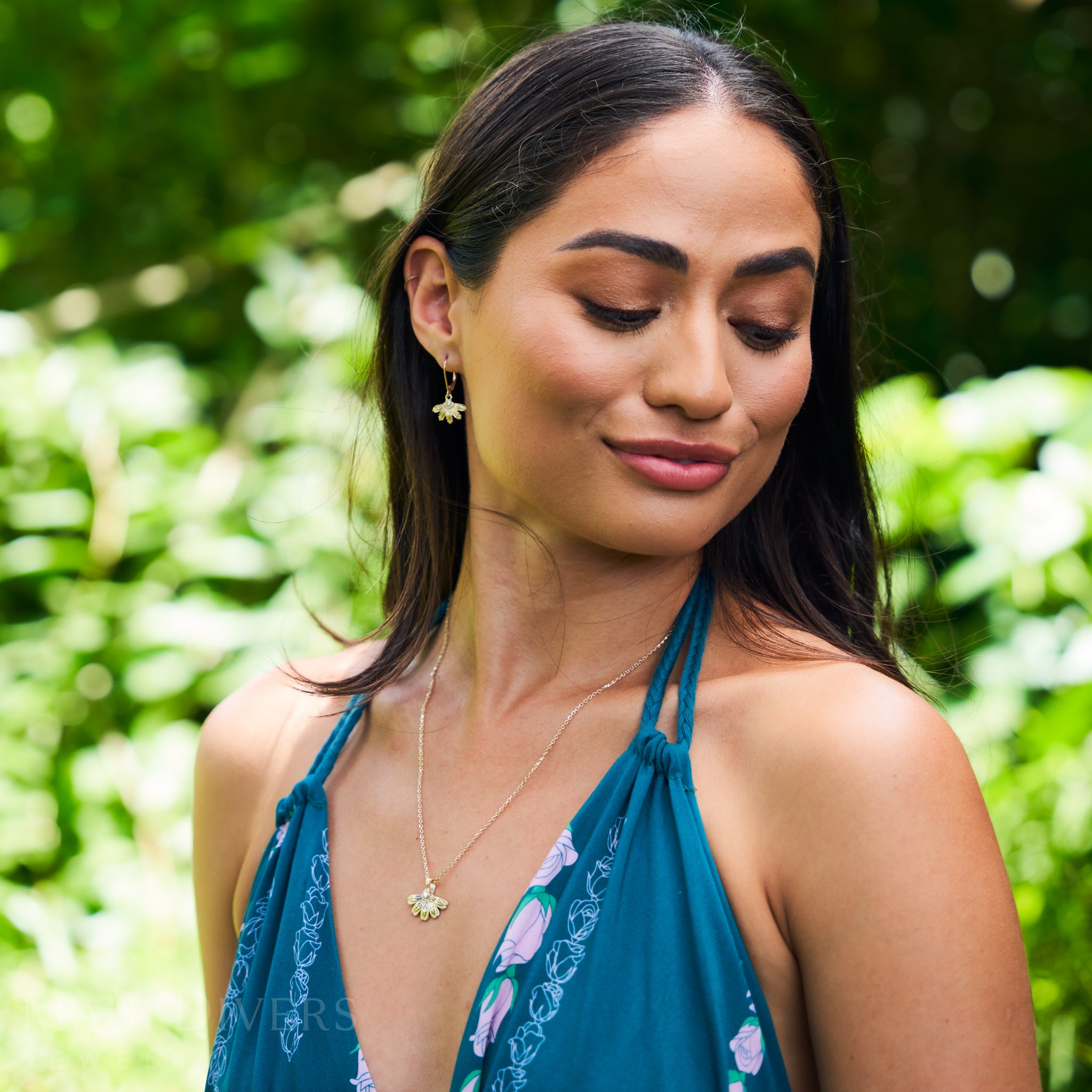 Woman in a garden wearing the Beach Naupaka Pendant and earrings in Gold with Diamonds
